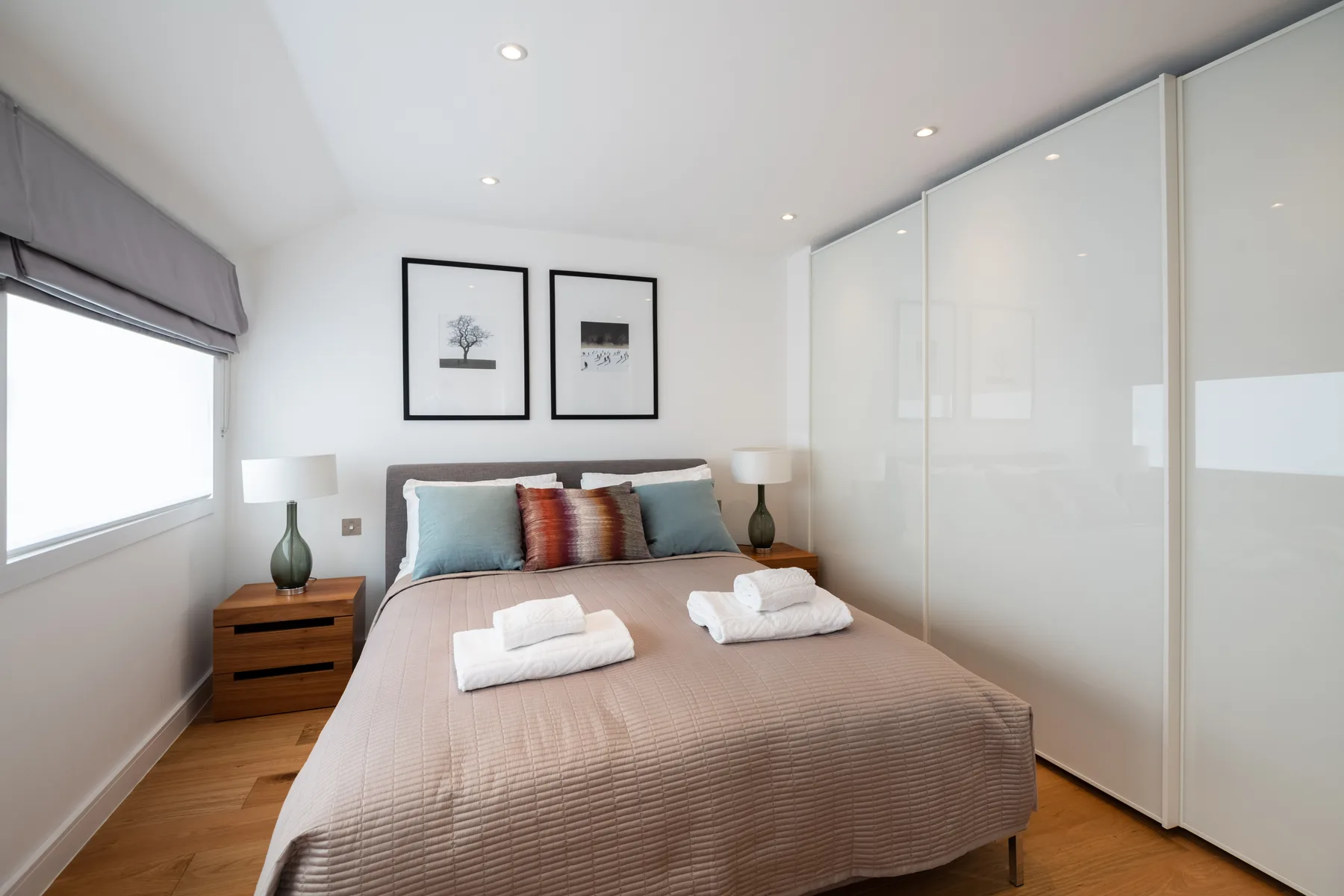 A bedroom with a neatly made bed, bedside tables, and framed artwork.