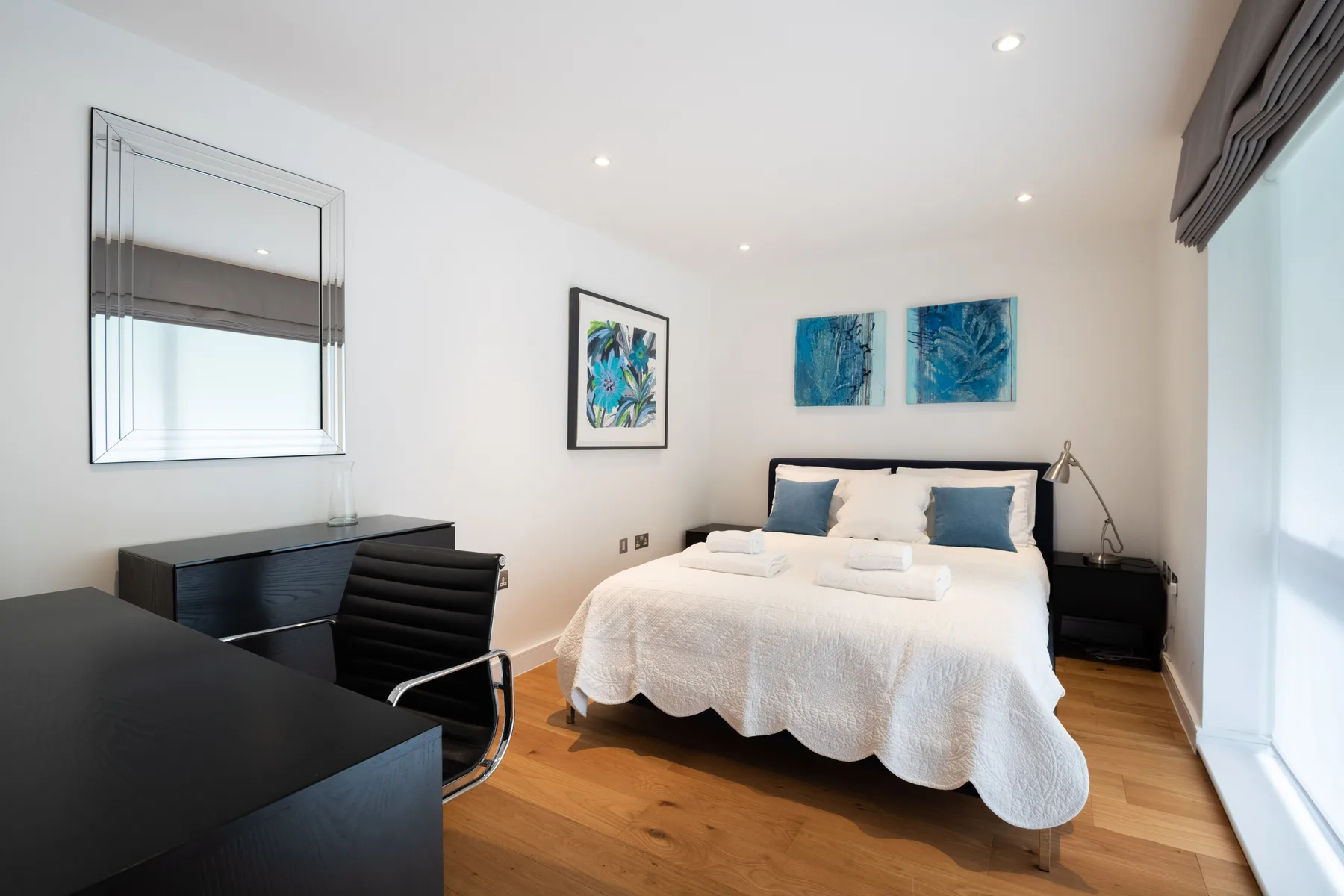 A bright bedroom with a neatly made bed and framed artwork on the walls.