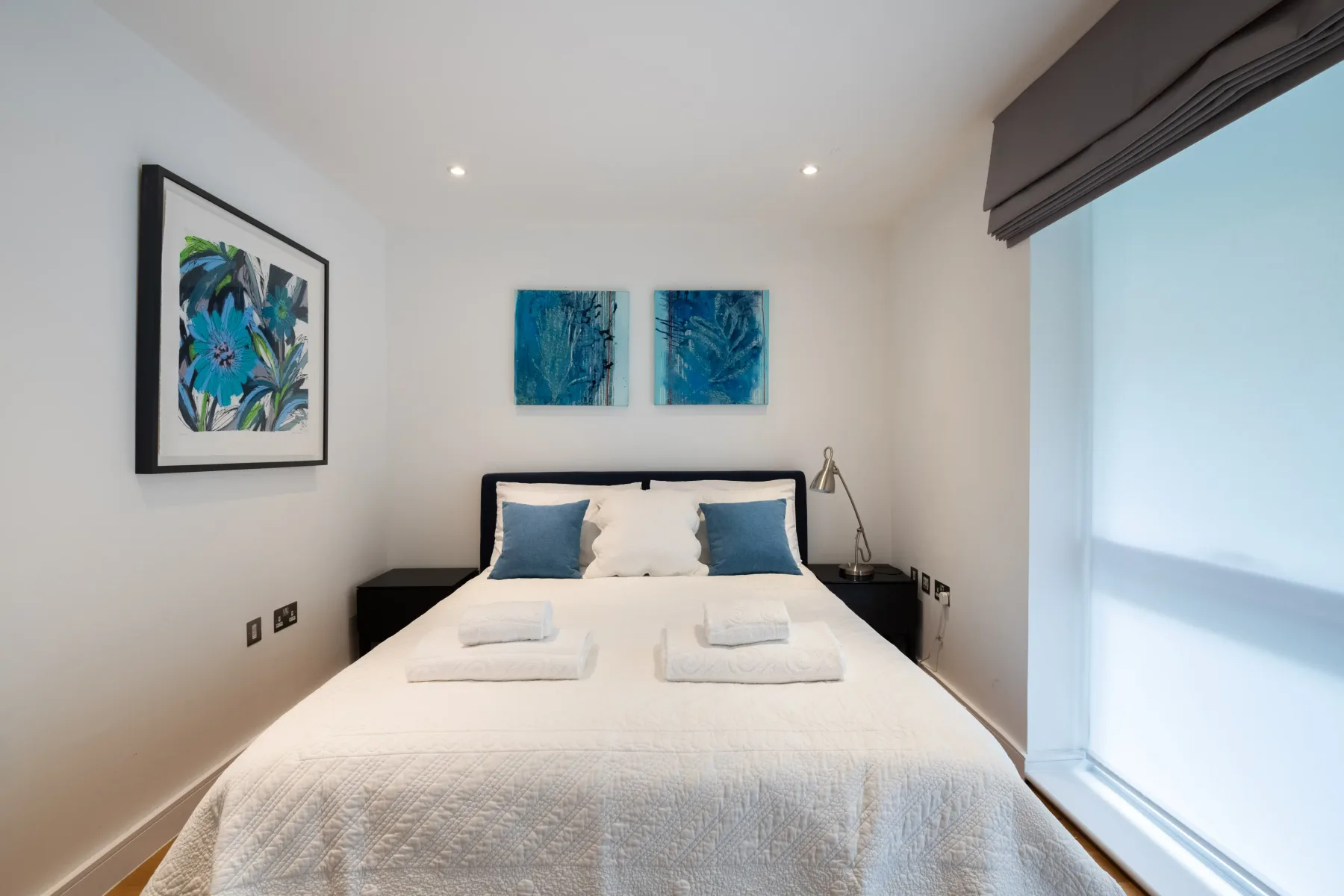A bright bedroom with a neatly made bed and blue botanical artwork.