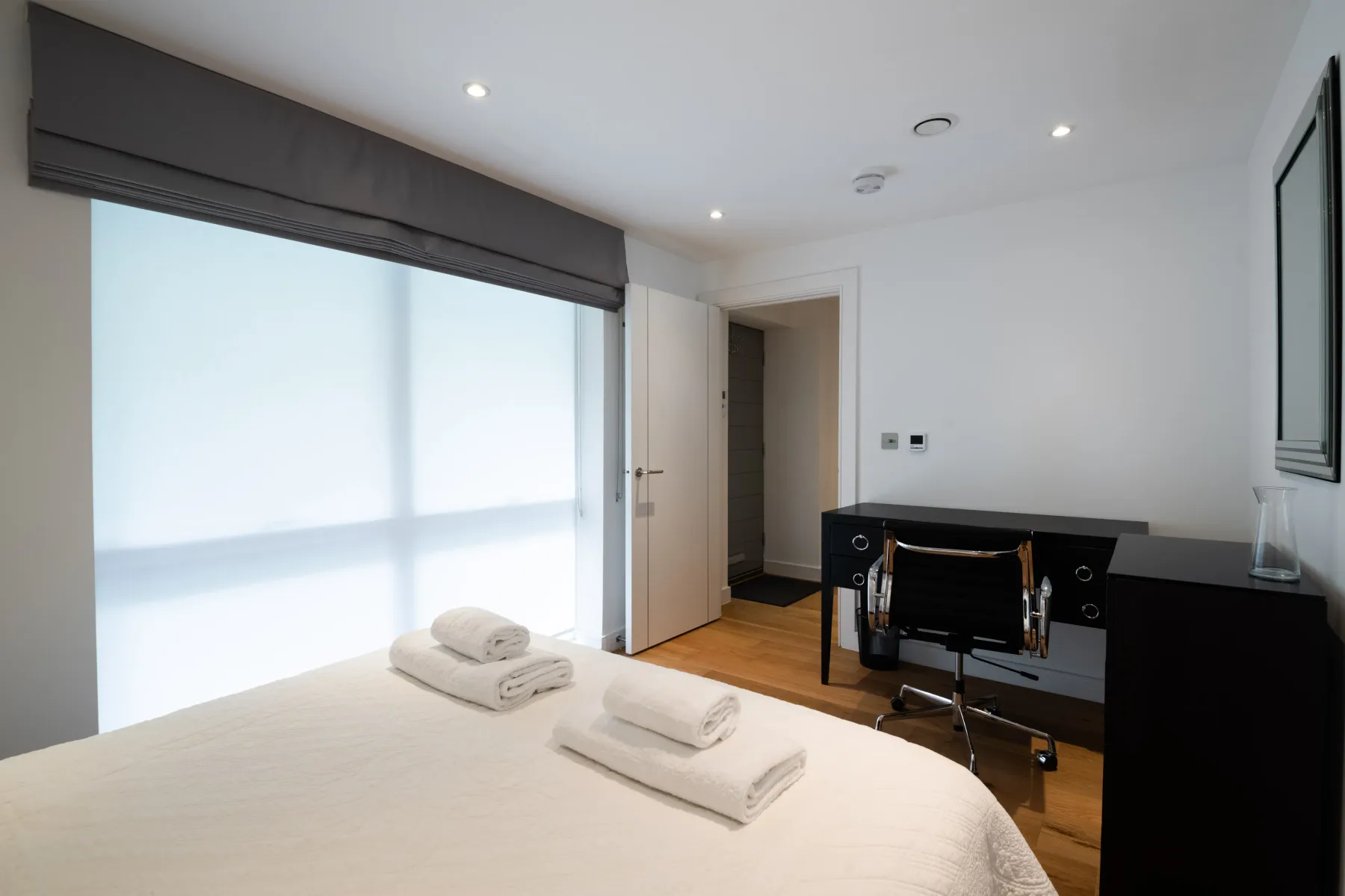 A bright bedroom with a desk and folded towels on the bed.