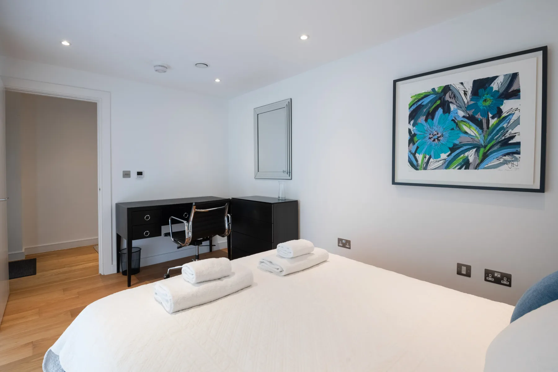 A bright bedroom with a neatly made bed and colorful wall art.