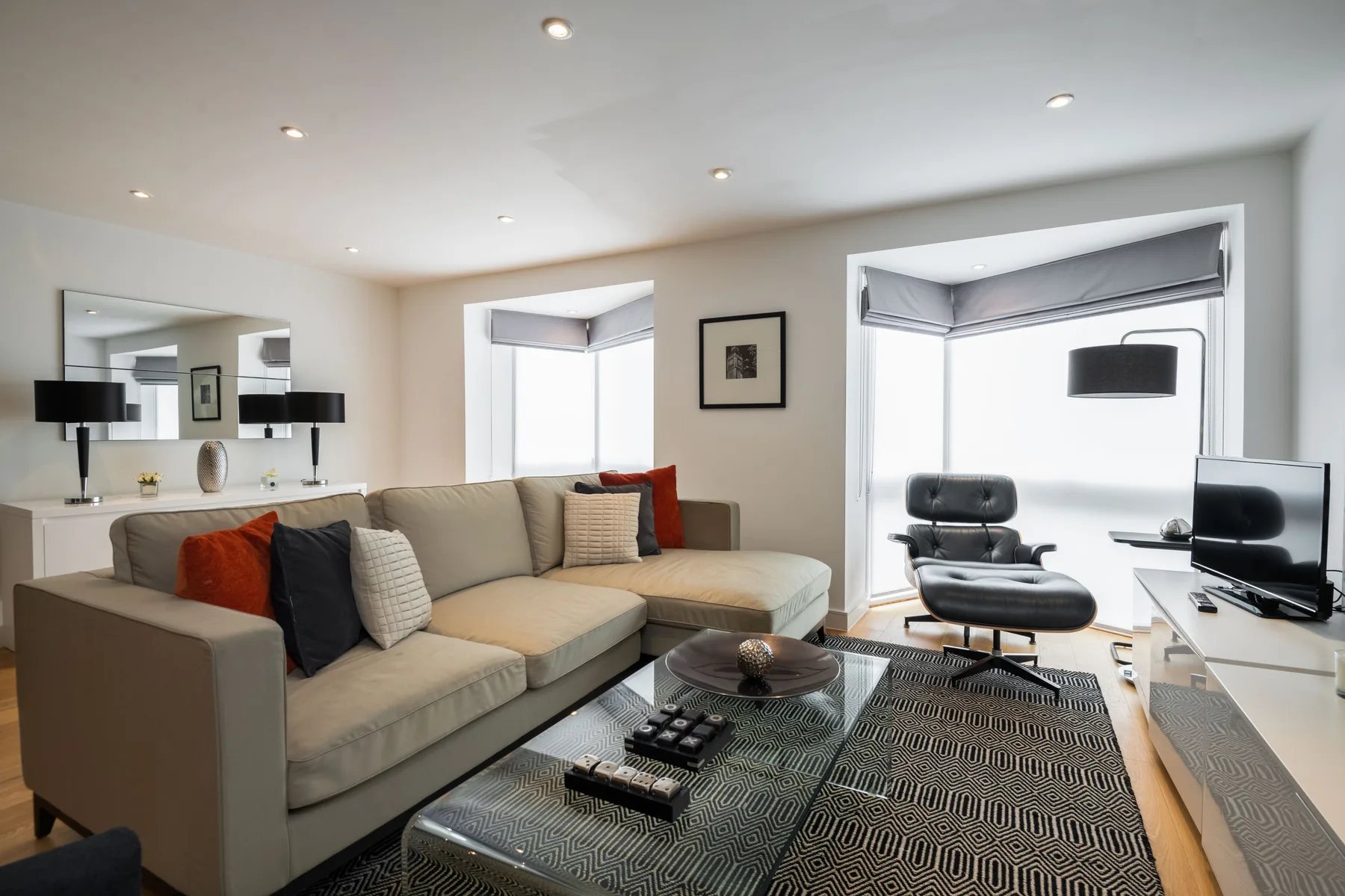 A bright living room with sectional seating, a glass coffee table, and large windows.