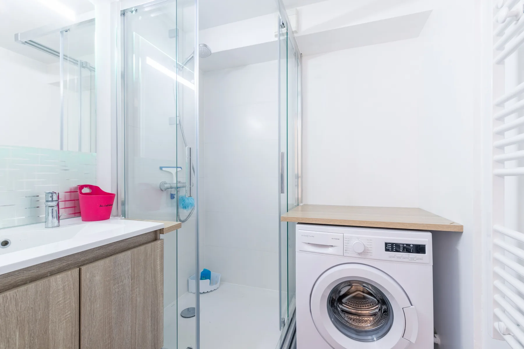 A bright bathroom with a shower, vanity, and washing machine.