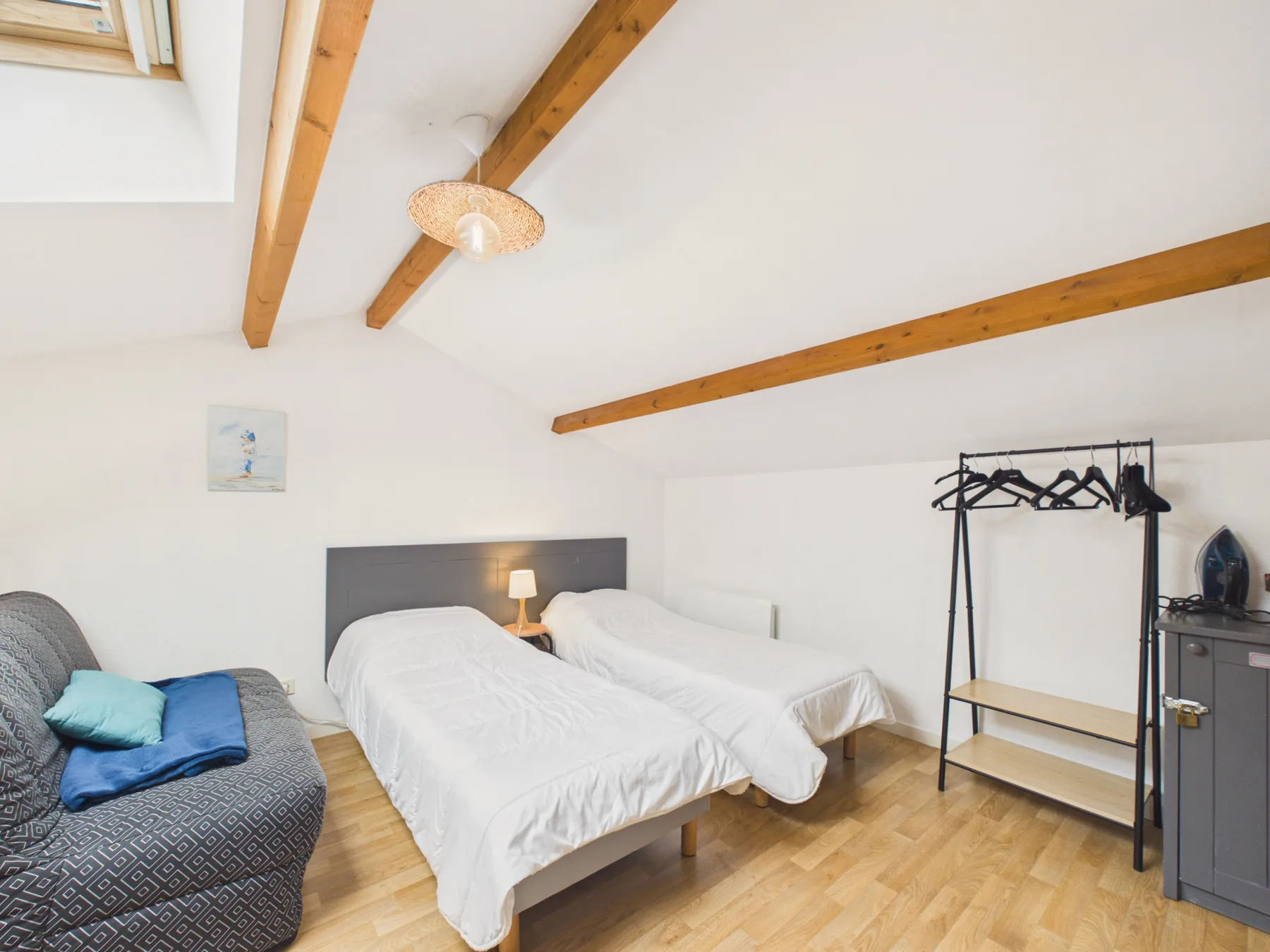 A bright bedroom with beds, a small sofa, and exposed ceiling beams.