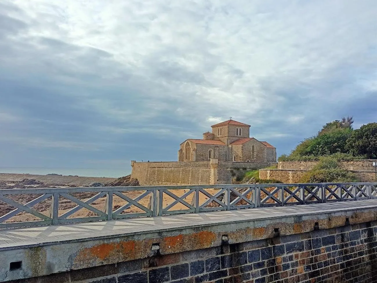 A stone church stands beside a coastal walkway and railing.