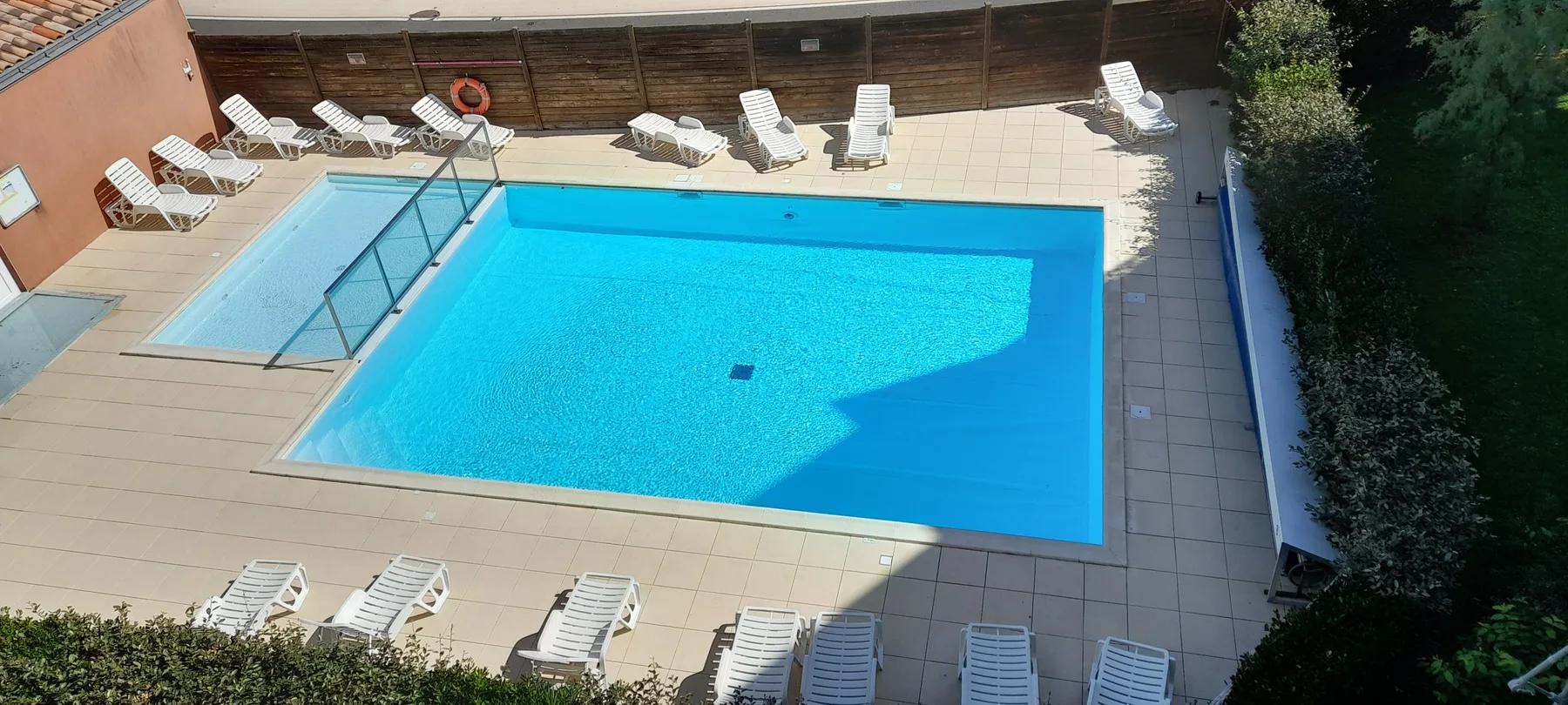 An outdoor swimming pool is surrounded by paved decking and lounge chairs.