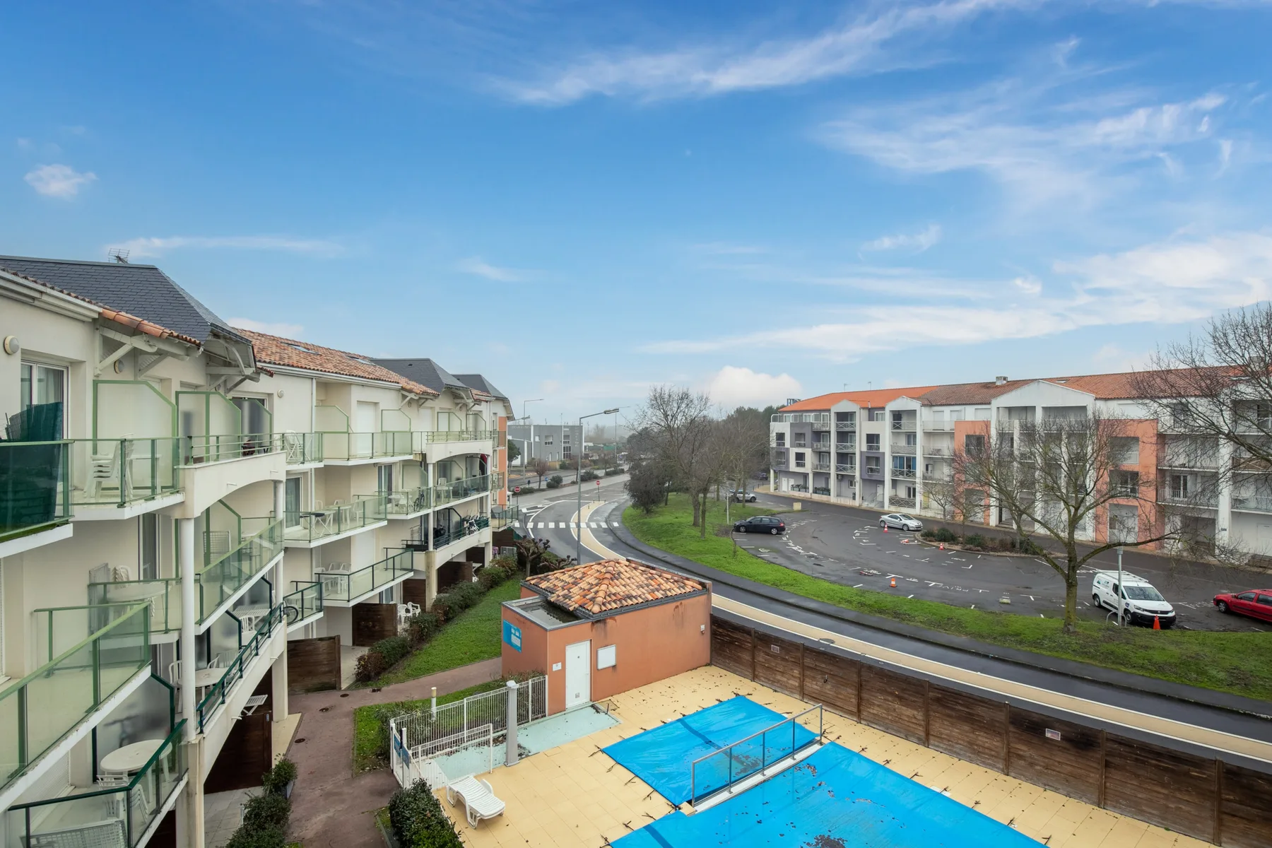 Apartment buildings overlook an outdoor swimming pool and a road.