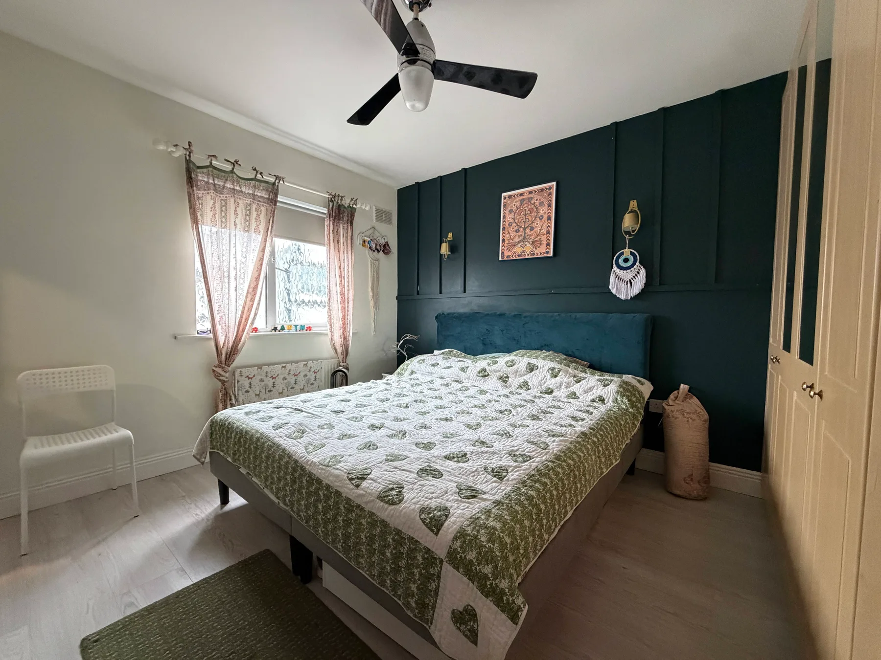 A bedroom with a patterned bedspread, dark accent wall, and window.