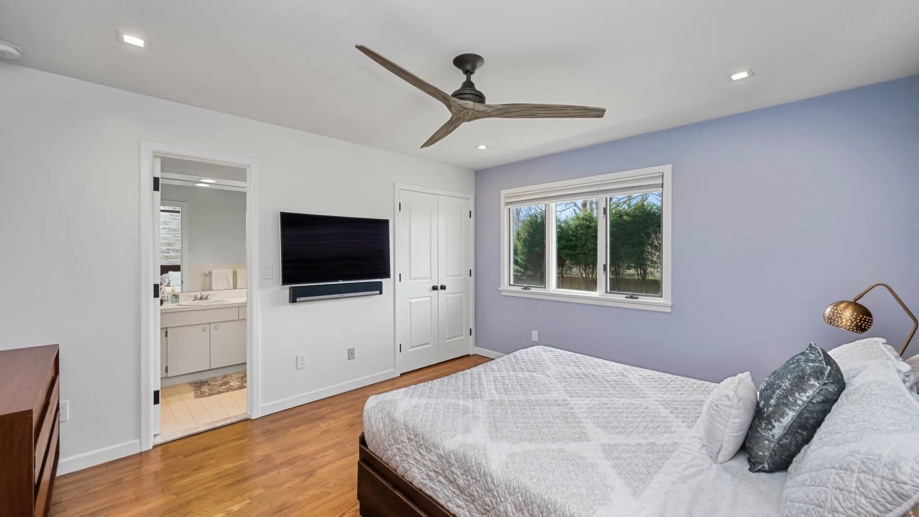 Un dormitorio luminoso con una cama, ventilador de techo y ventana amplia.