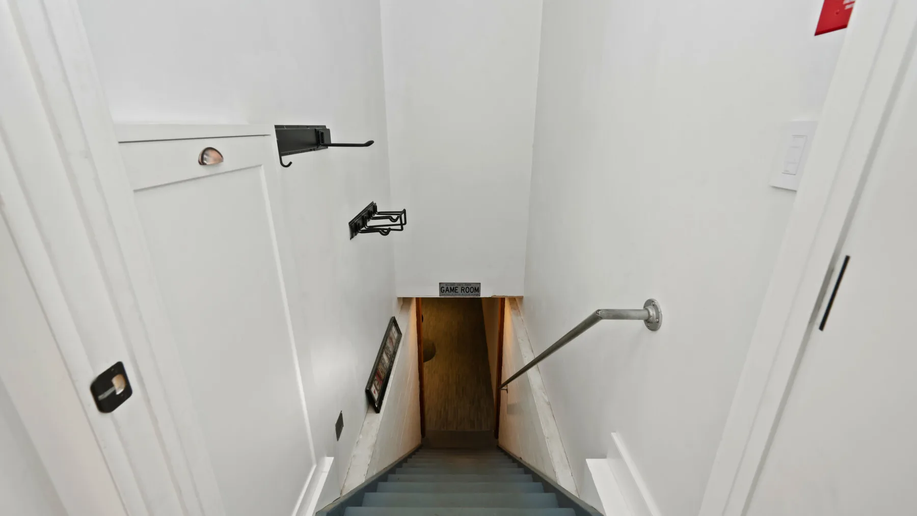 Una estrecha escalera interior baja entre paredes blancas y tiene un pasamanos metálico.