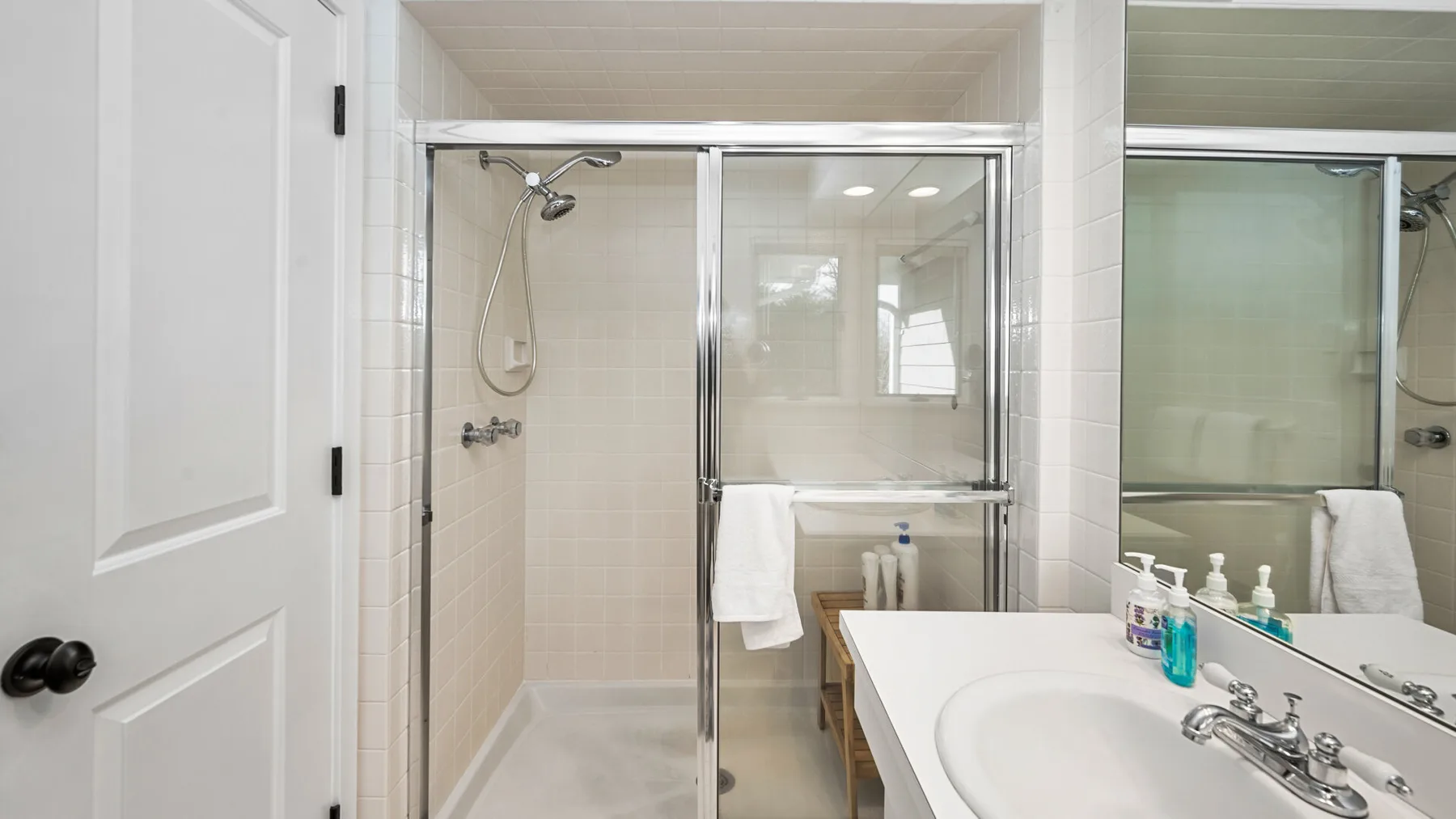 Un baño luminoso con una ducha de vidrio y un lavabo blanco.