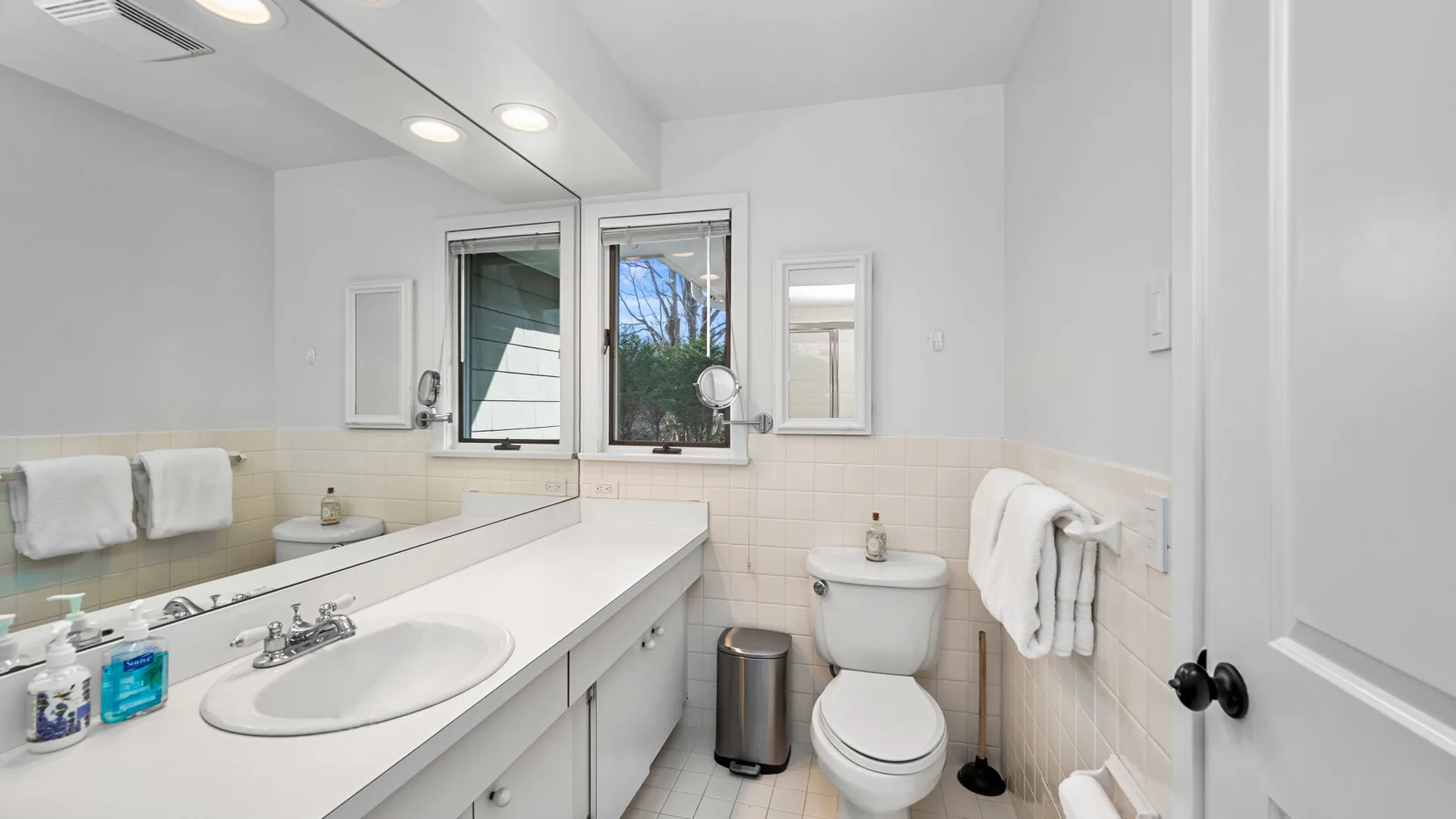 Un baño luminoso con una encimera larga con lavabo, inodoro y ventana.