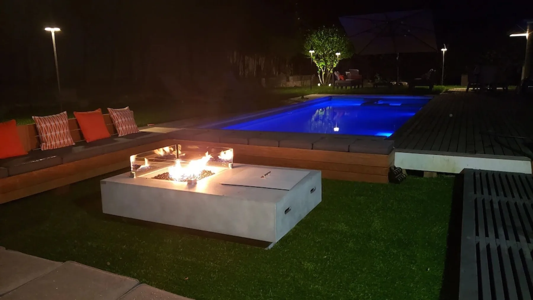 Zona de piscina al aire libre por la noche, con una fogata encendida y asientos.