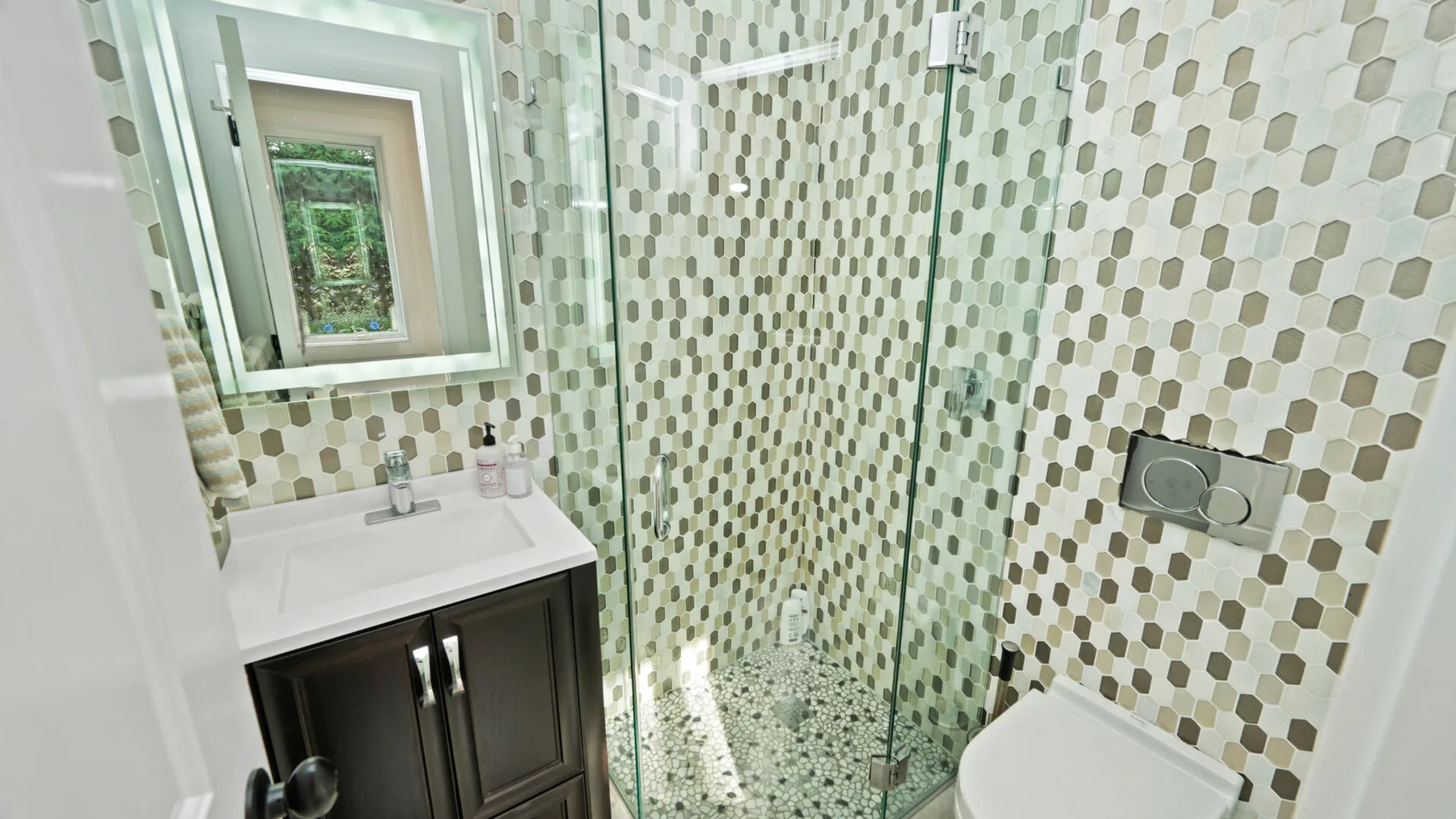 Un baño con lavabo, inodoro y ducha de vidrio junto a una pared de azulejos estampados.