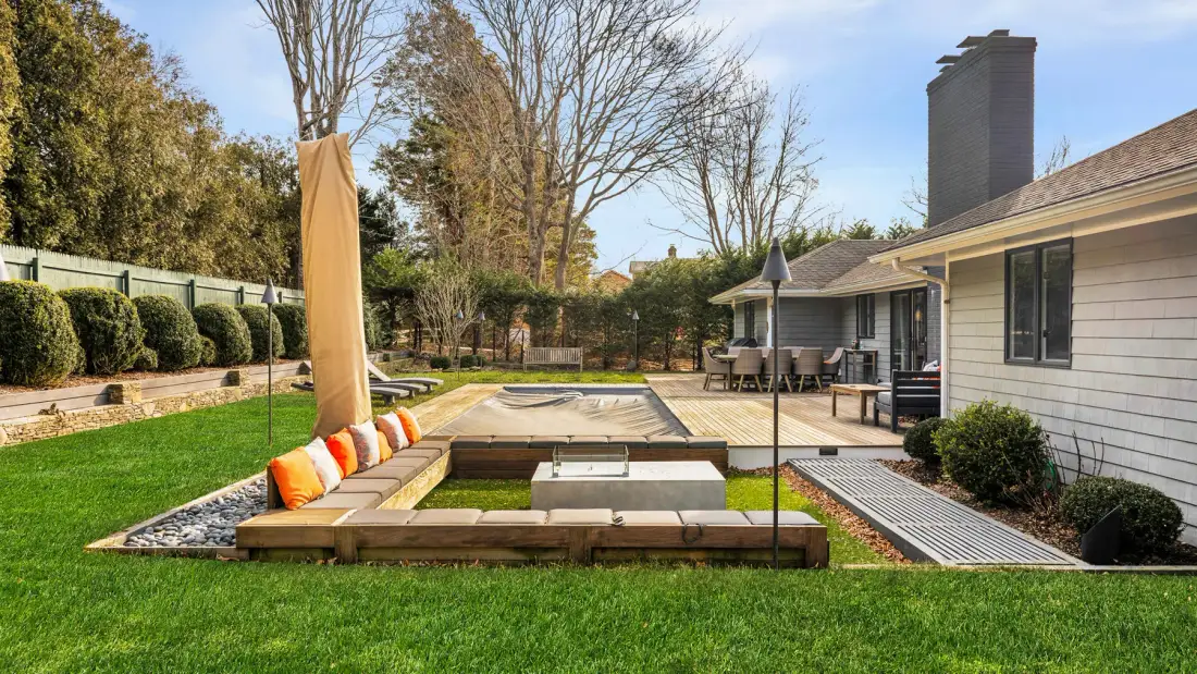 Un patio trasero con asientos integrados rodea una estructura rectangular hundida para fuego.