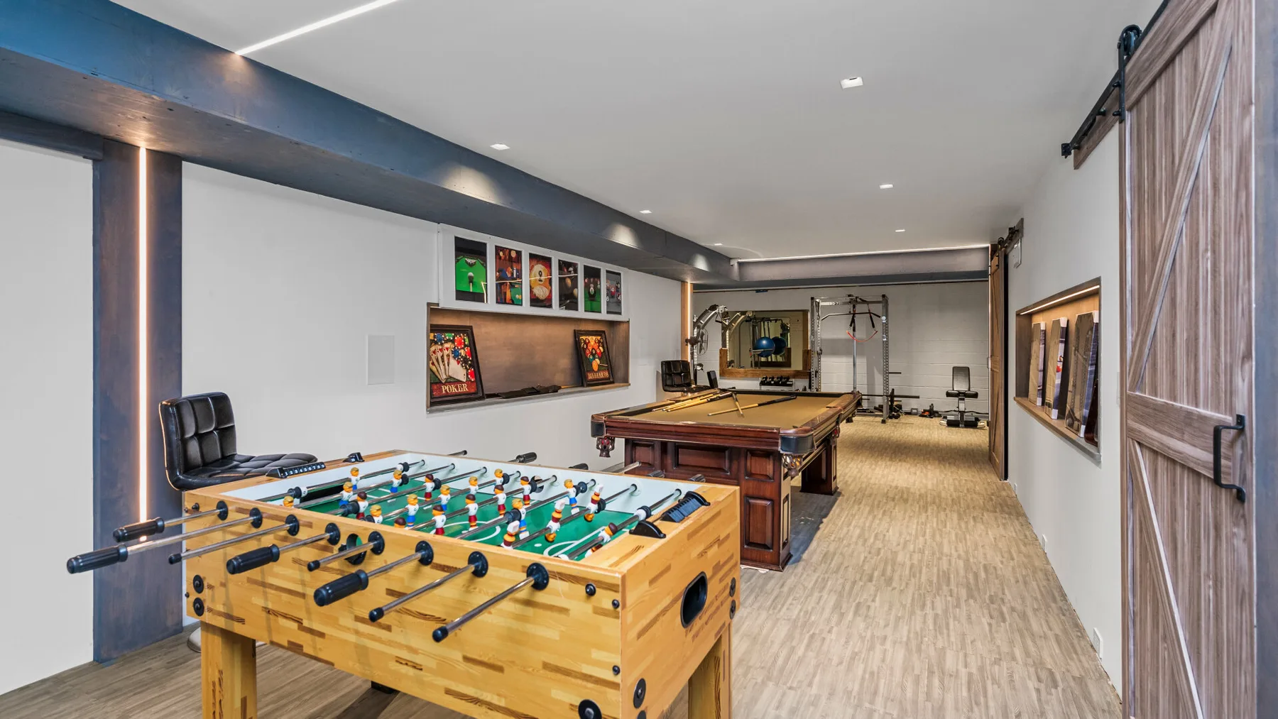 Una sala de juegos con un futbolín en primer plano y una mesa de billar detrás.