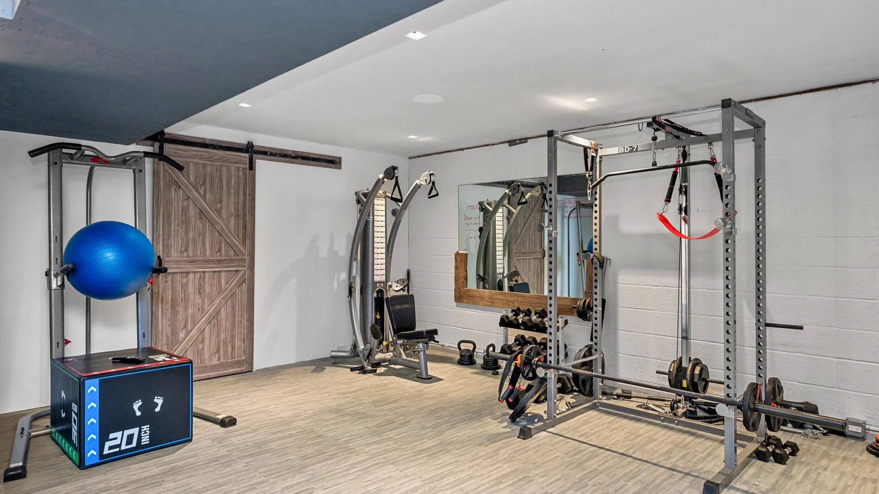 Un gimnasio en casa con máquinas de ejercicio, pesas y una pelota azul.