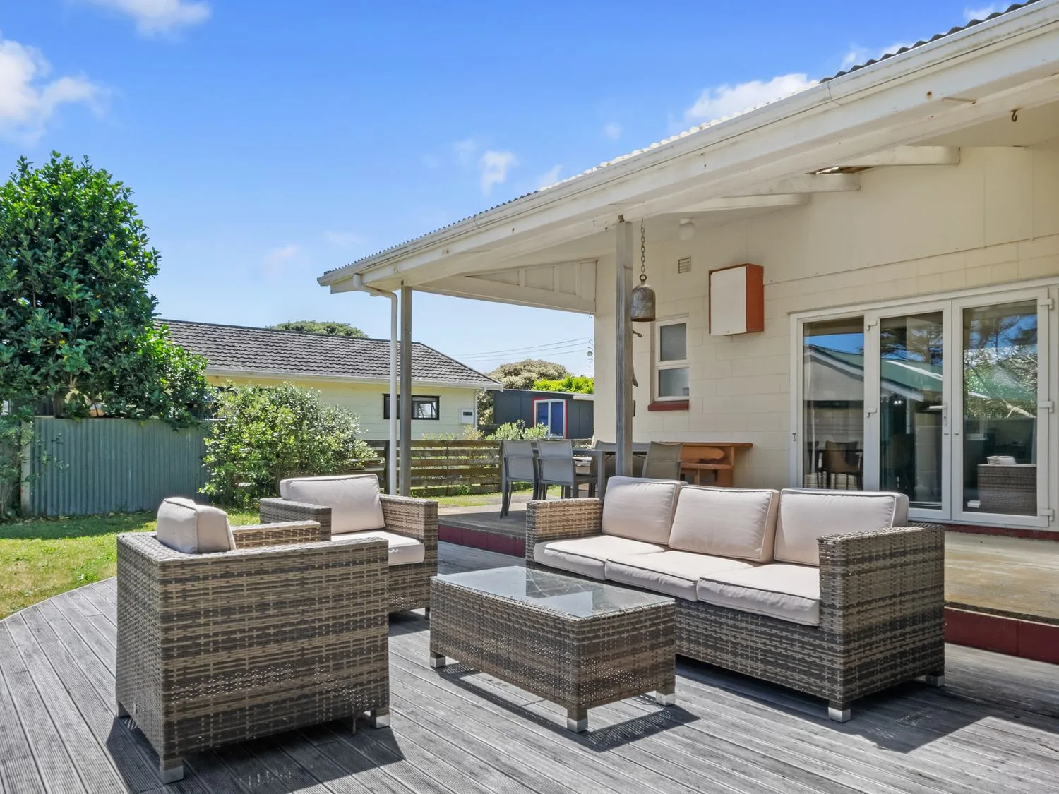Un patio al aire libre con muebles de asiento de estilo mimbre, incluidos un sofá y sillas con cojines, y una mesa de centro con superficie de vidrio en Sunlit Retreat - Te Horo Beach Holiday Home, en Te Horo Beach