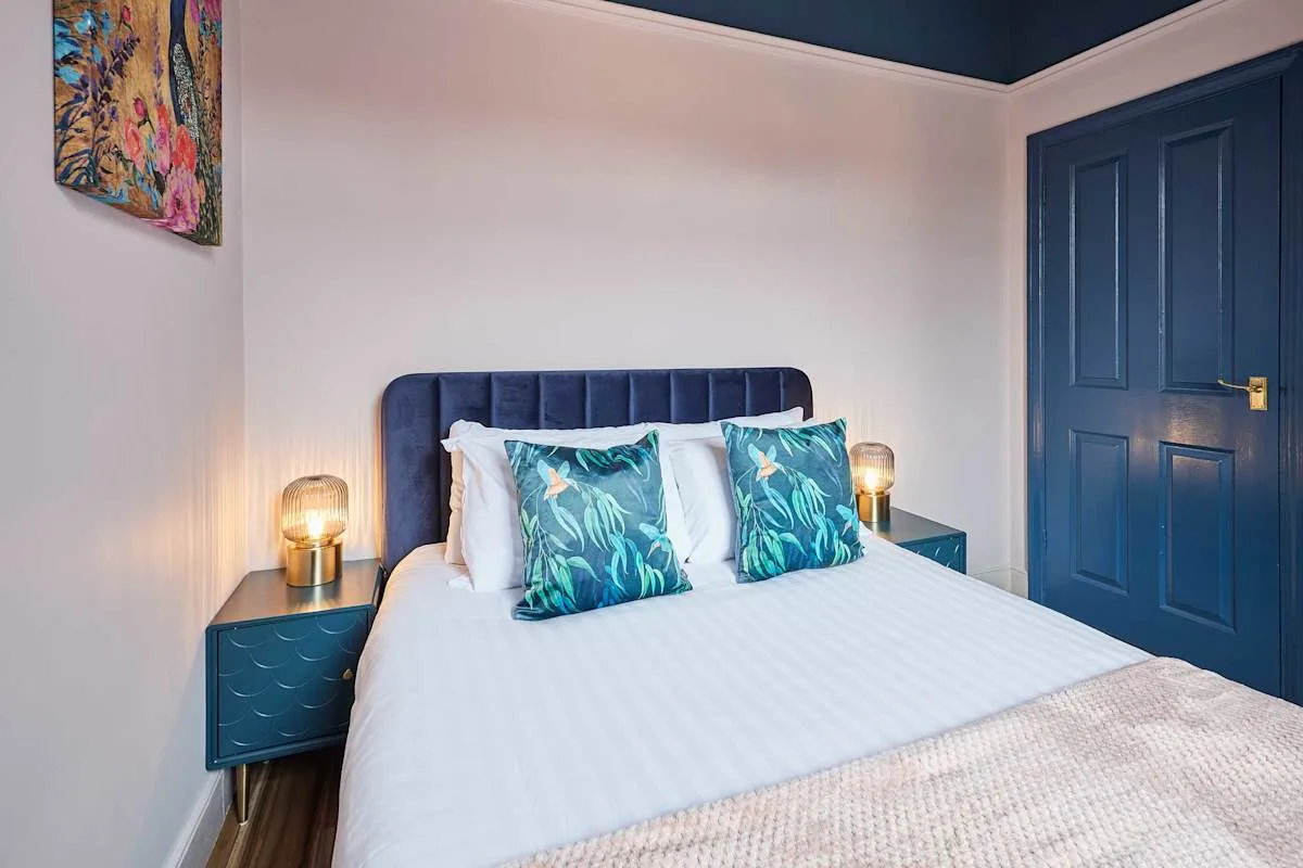 Un dormitorio con una cama bien tendida y mesitas de noche color turquesa.