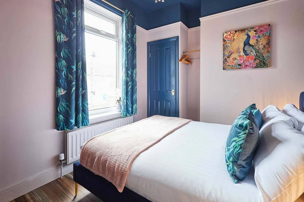 Un dormitorio con una cama, una puerta azul y una ventana con cortinas estampadas.