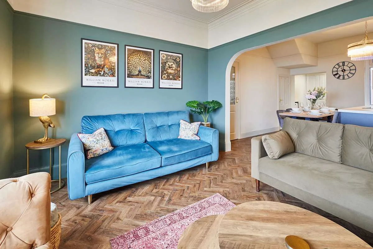 Sala de estar con asientos azules, cuadros en la pared y un comedor contiguo.