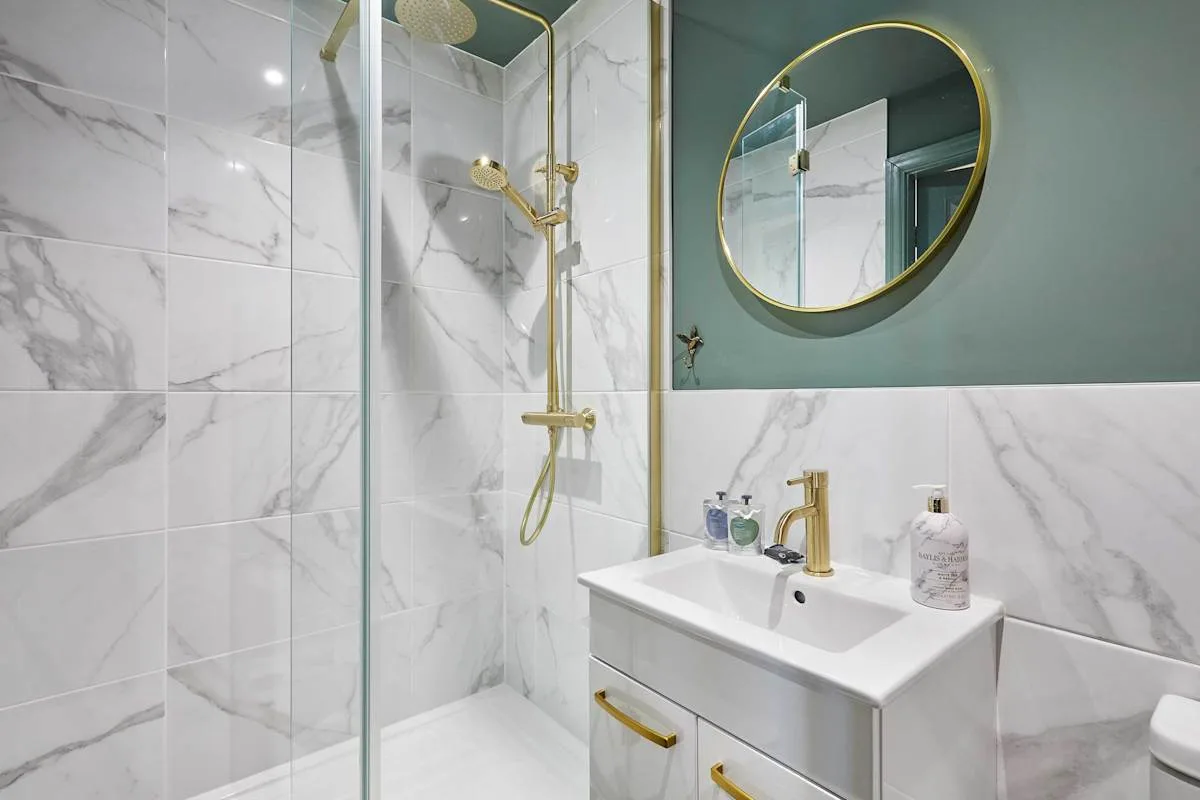 Un baño con azulejos, una ducha de vidrio y un lavabo bajo un espejo redondo.