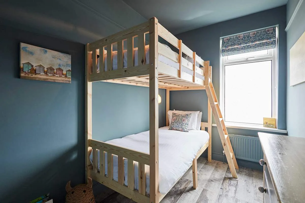 Un dormitorio con una litera de madera junto a una ventana luminosa.