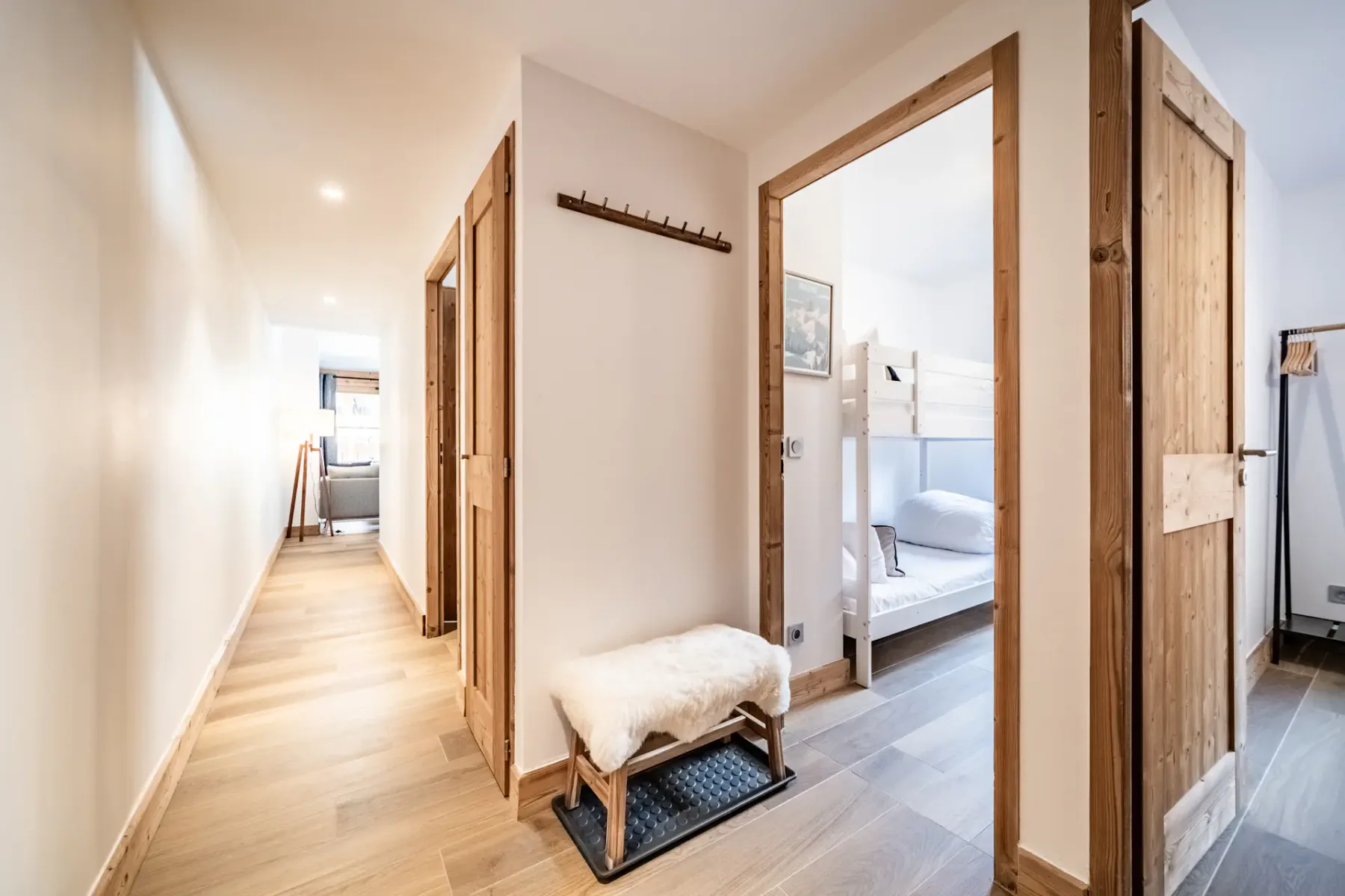 Small room with wooden bunk beds, white bedding, a window showing an outside view, and a black metal shelf against a white wall.