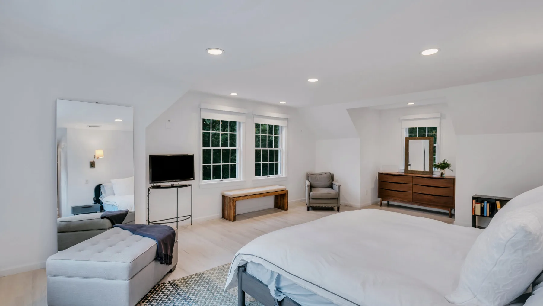 A bright bedroom with a large bed, a seating area, and two windows.