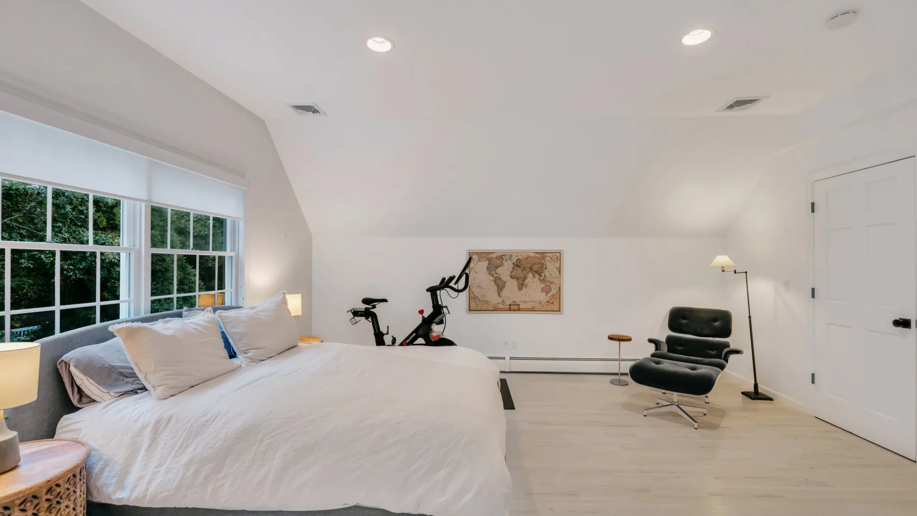 A bright bedroom with a large bed, windows, and a seating area.