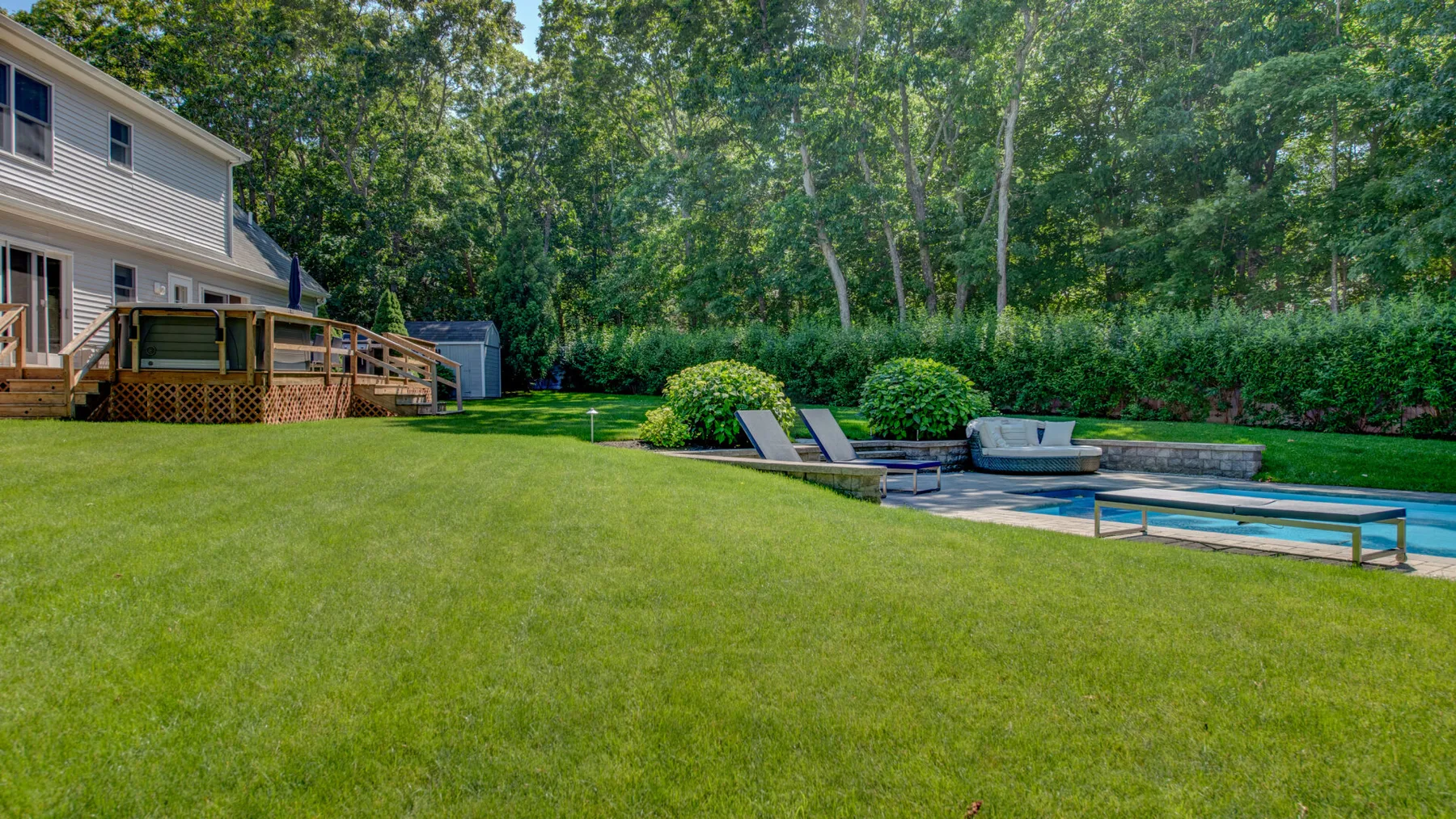 A grassy backyard with a deck, lounge seating, and a swimming pool.