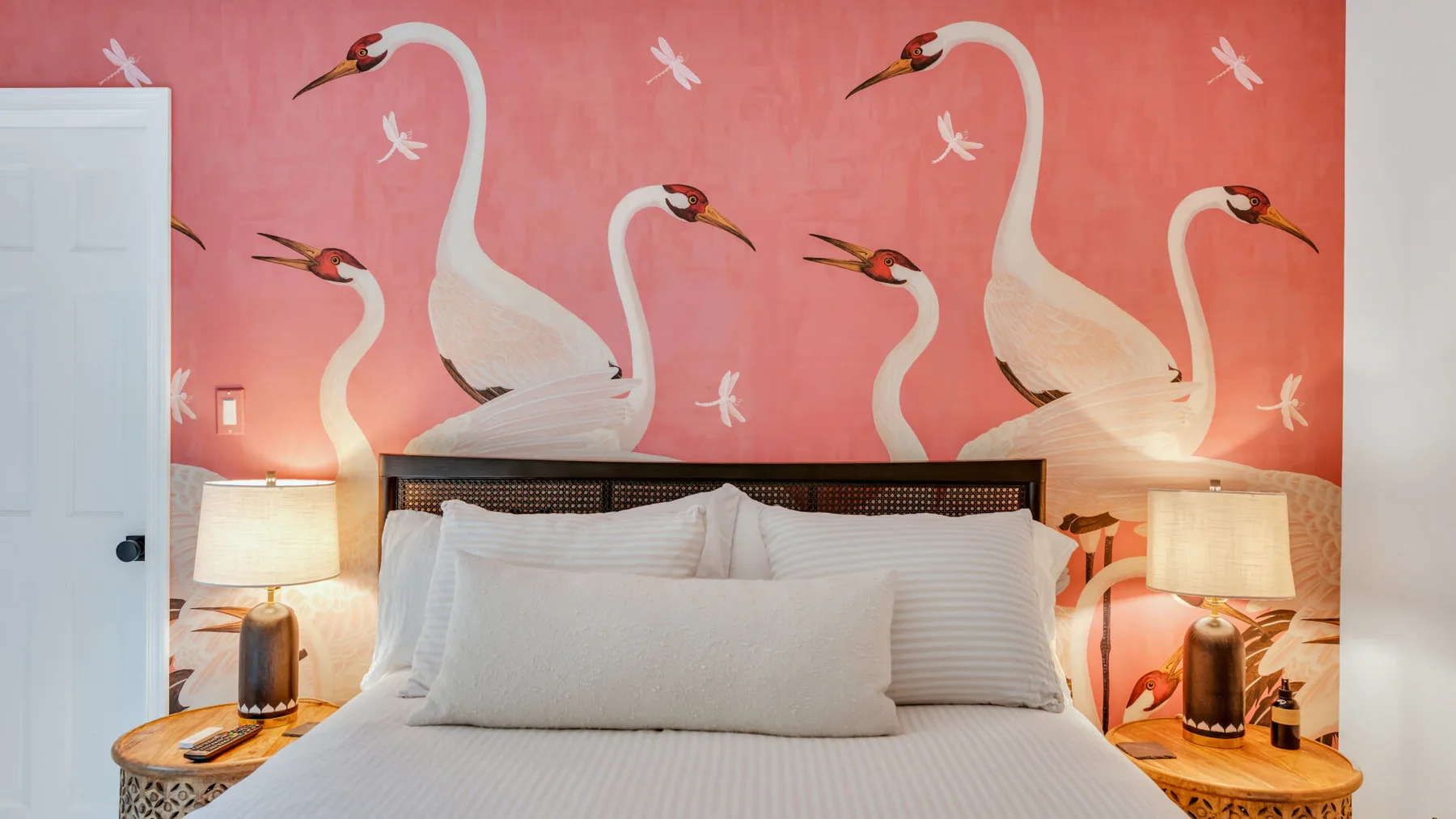 A bedroom with a white bed beneath a pink wall painted with birds.