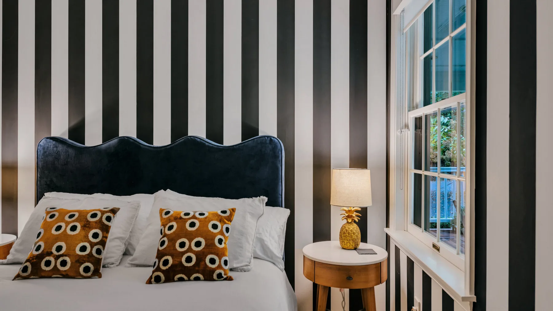 A bedroom with a bed, patterned pillows, and a window beside a small table.