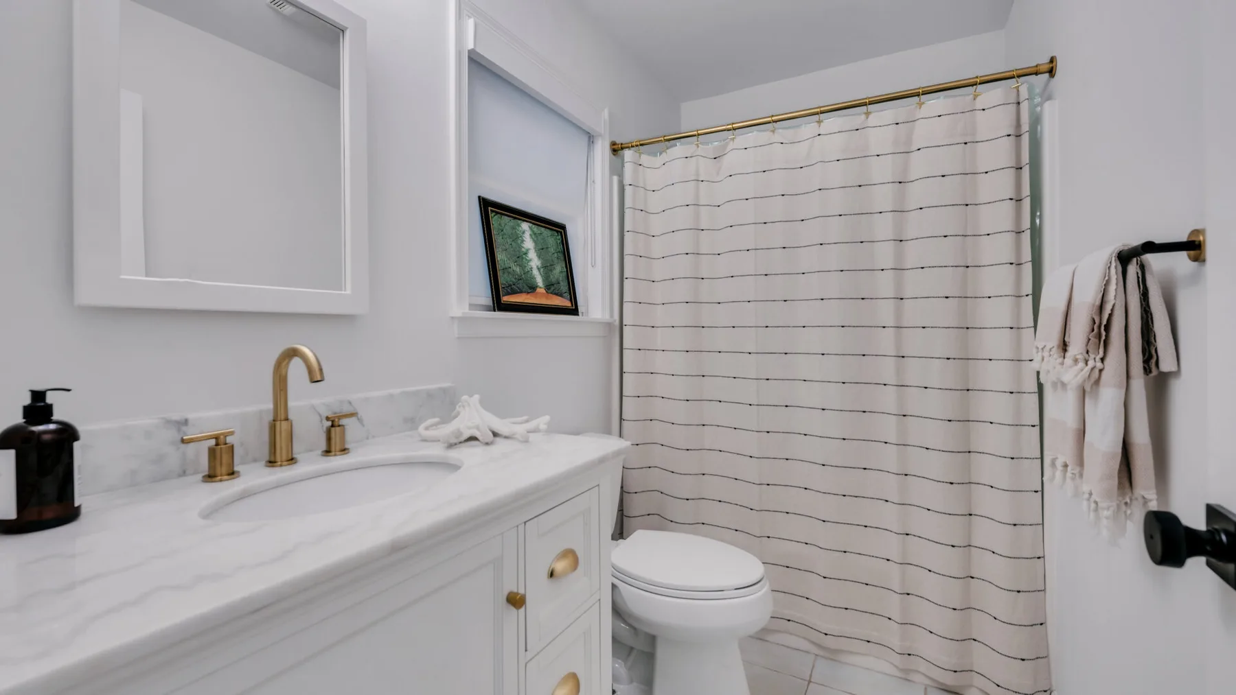 A bright bathroom with a white vanity, toilet, and striped shower curtain.