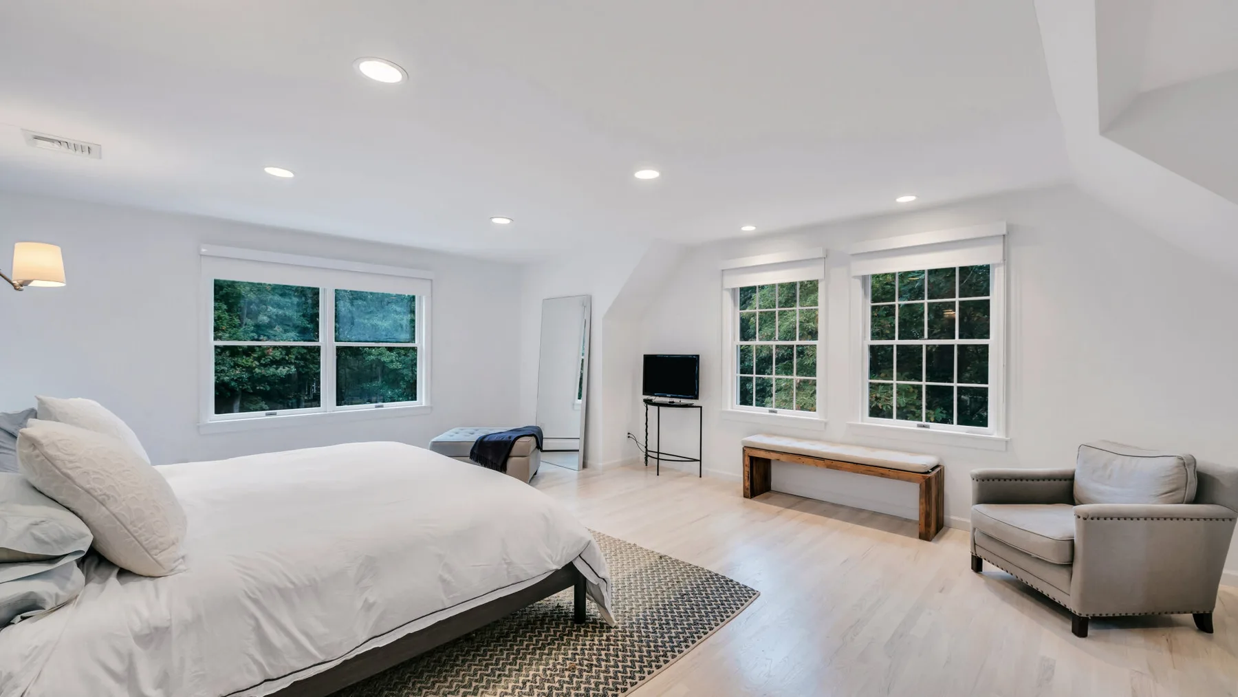 A bright bedroom with a large bed, several windows, and a small seating area.