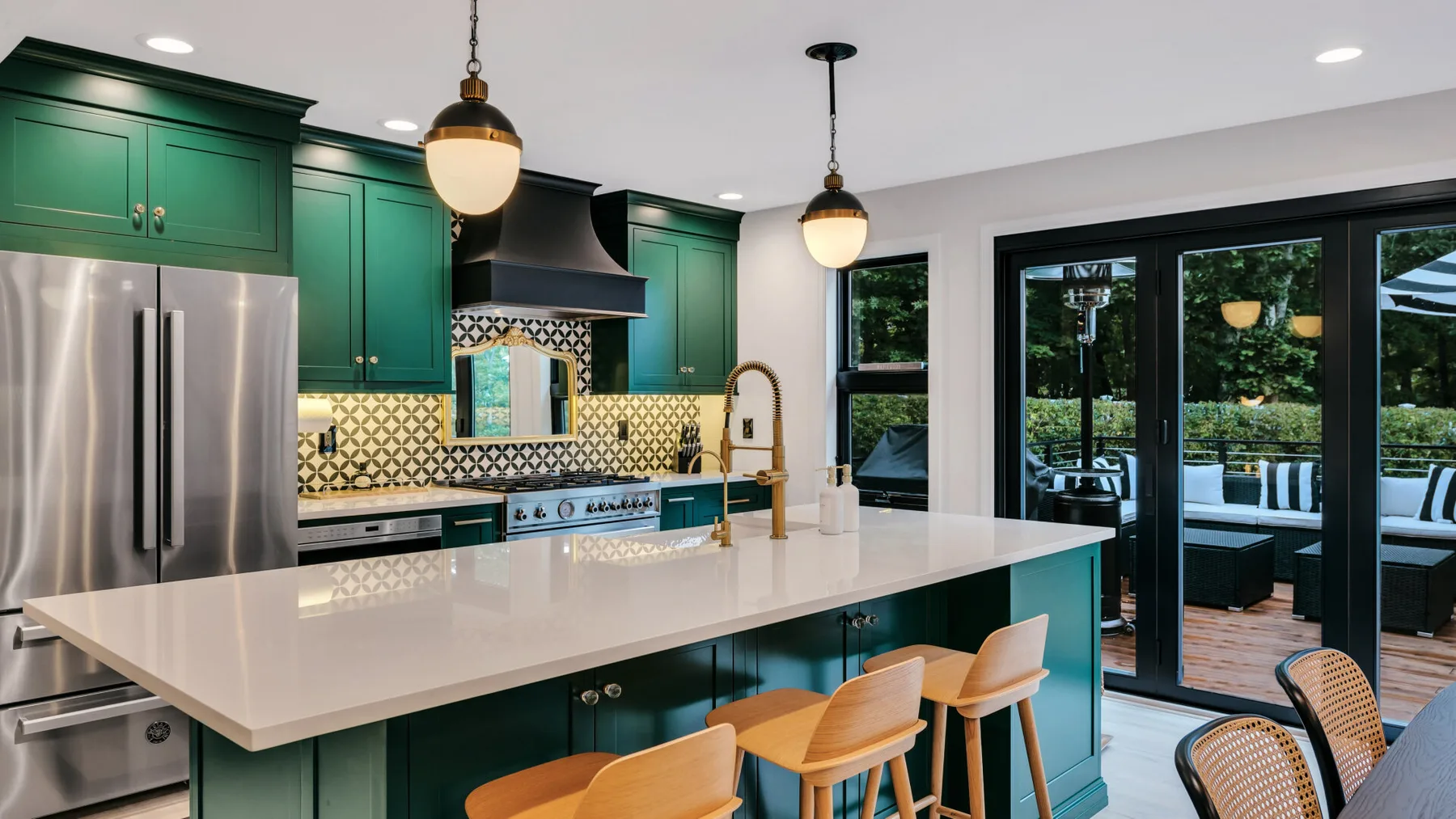 A modern kitchen with green cabinets, a large island, and glass doors opening to a garden.