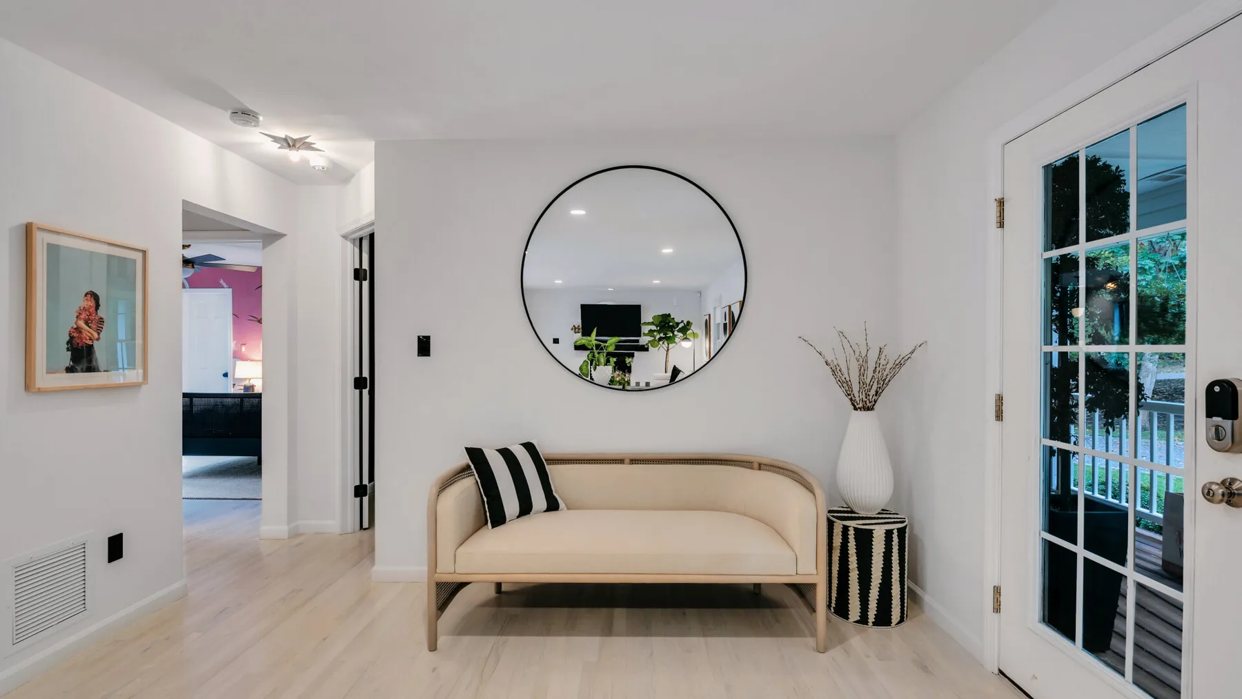 A bright living room with a curved sofa beneath a round wall mirror.