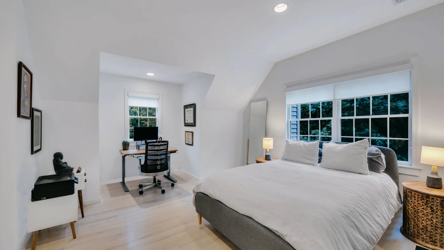 A bright bedroom with a large bed and a desk beside the windows.