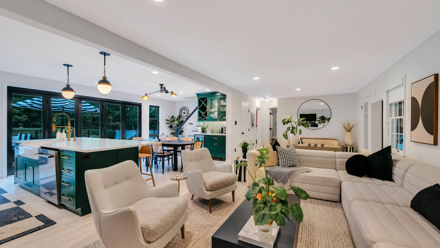 An open-plan living room and kitchen with light seating and green cabinetry.