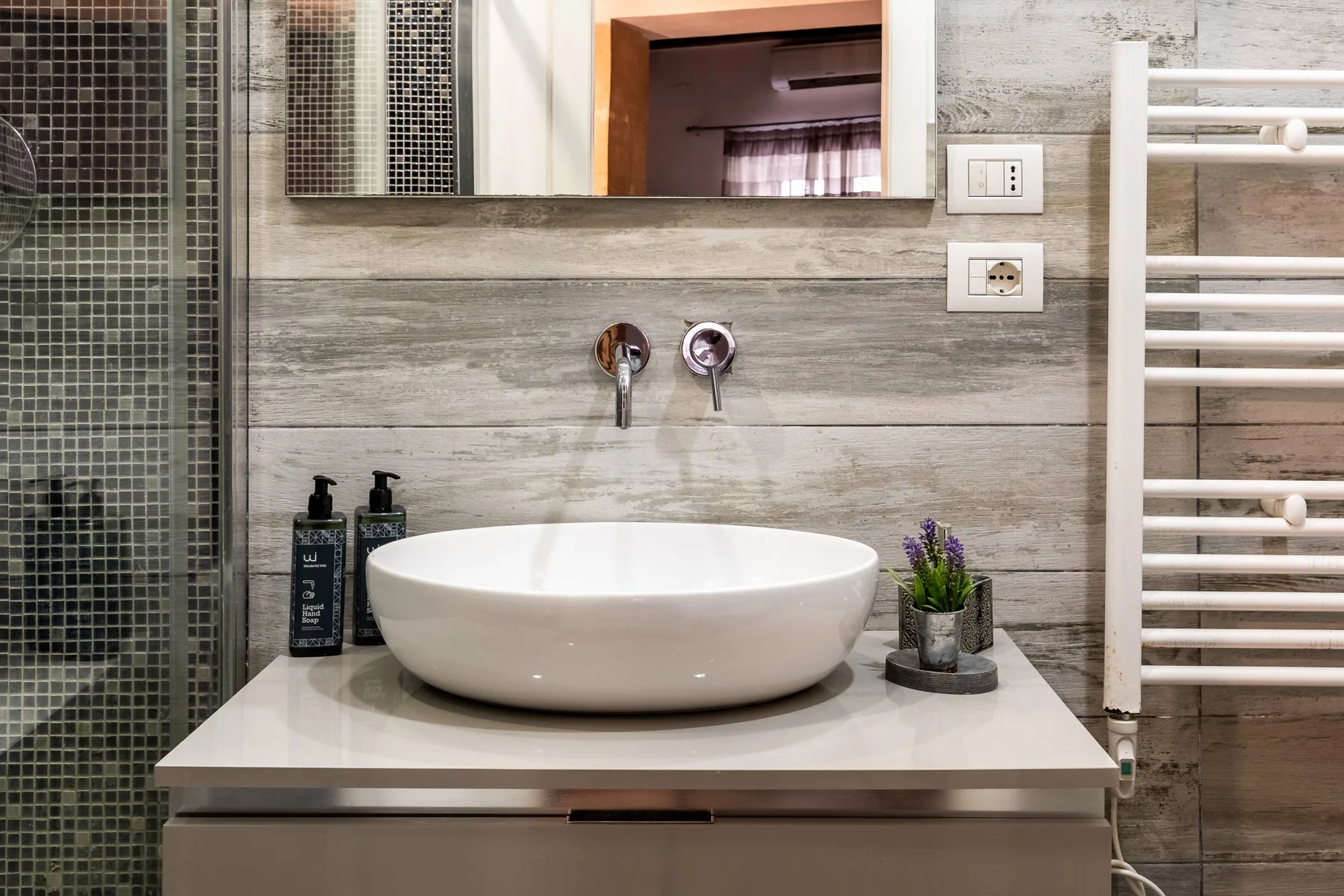 Un tocador de baño con lavabo sobre encimera, grifería mural y ducha con azulejos.