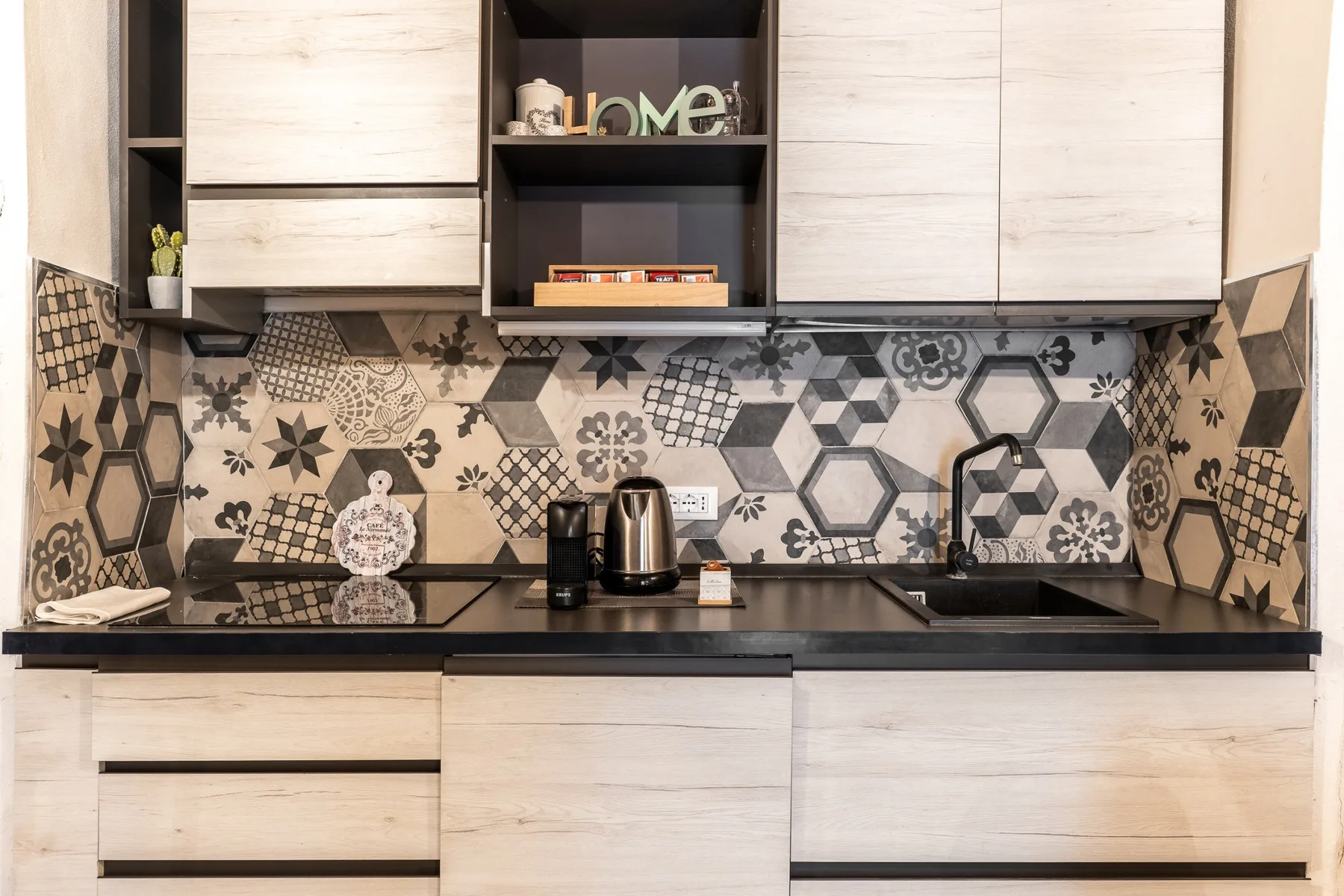 Una cocina moderna con gabinetes claros, encimera oscura y salpicadero de azulejos estampados.