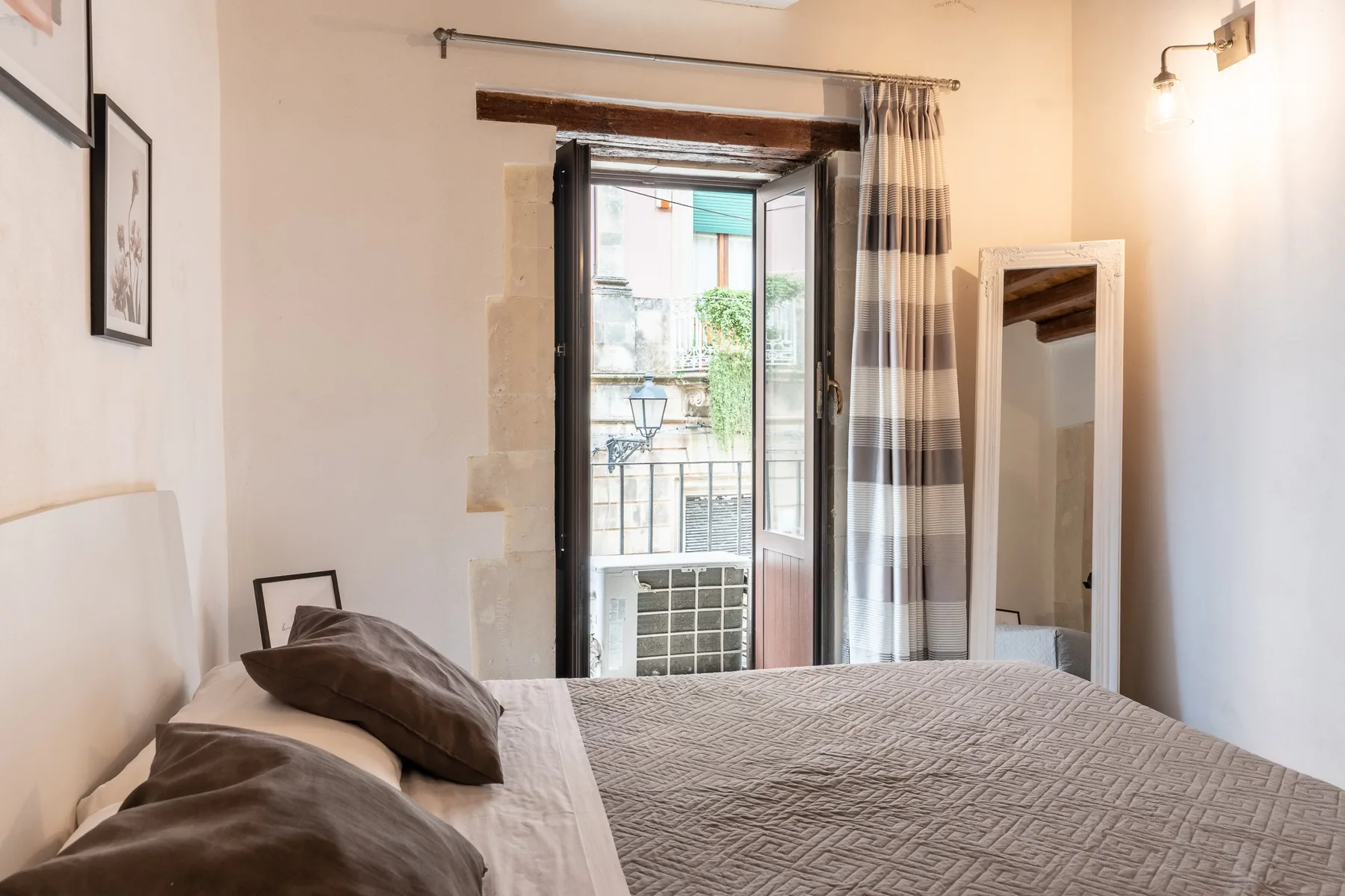 Un dormitorio con una cama junto a una ventana abierta y cortinas a cuadros.