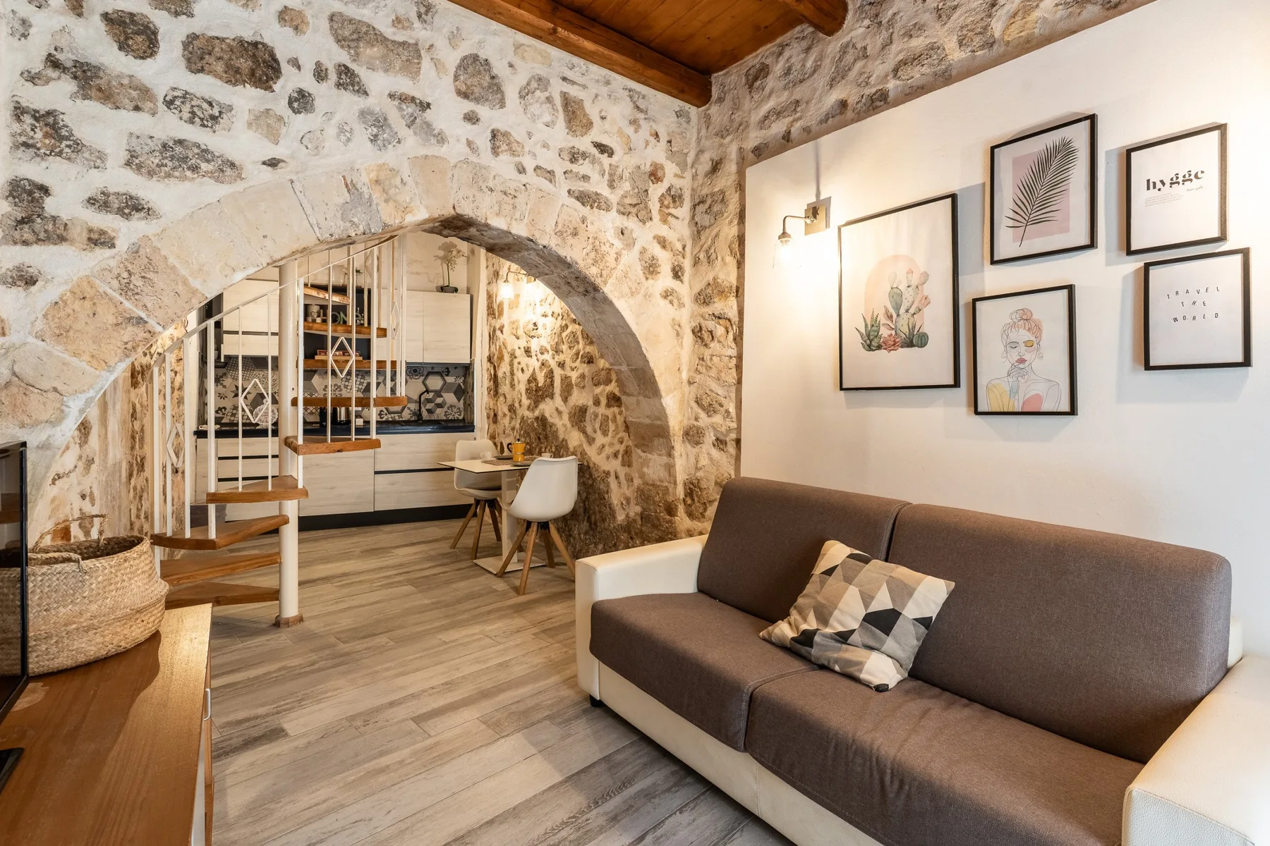 Una sala de estar con sofá, cuadros y un arco de piedra que da a la cocina.