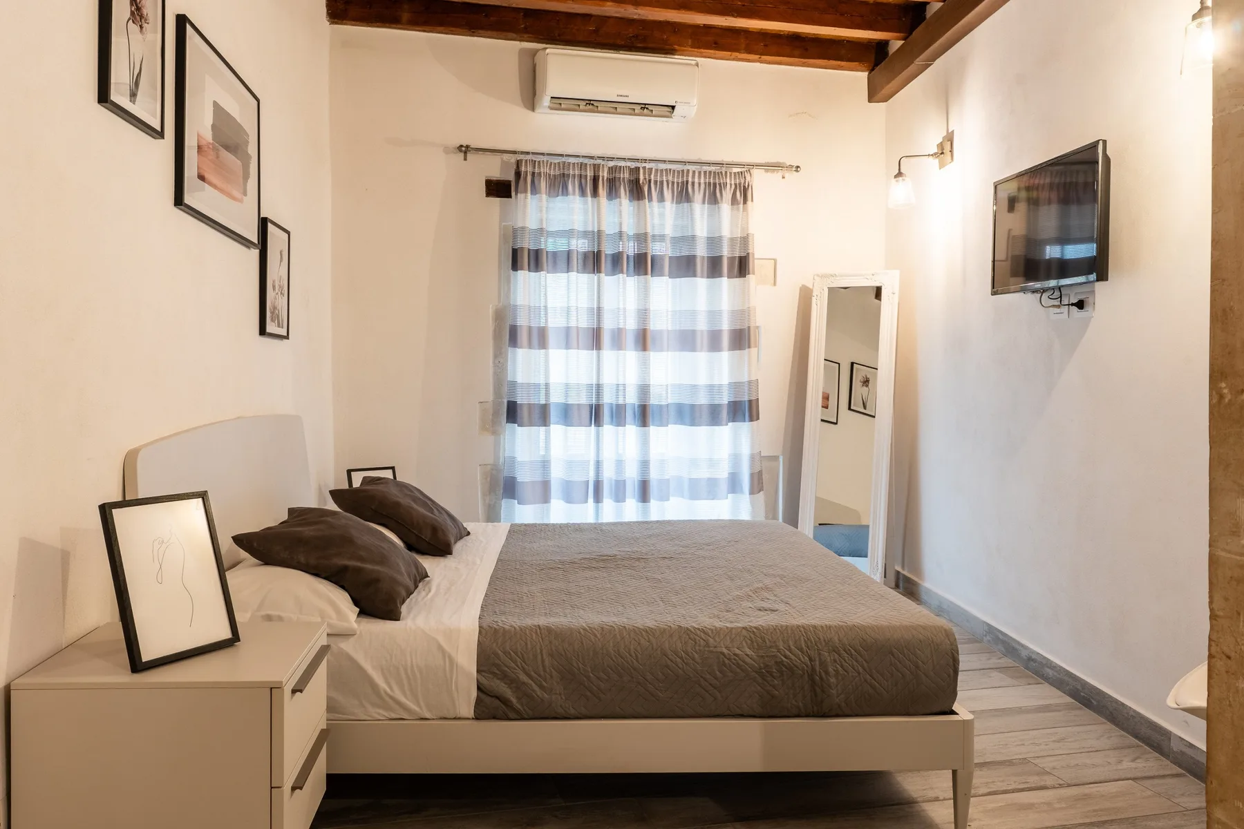 Un dormitorio con una cama, cortinas a rayas y un televisor en la pared.
