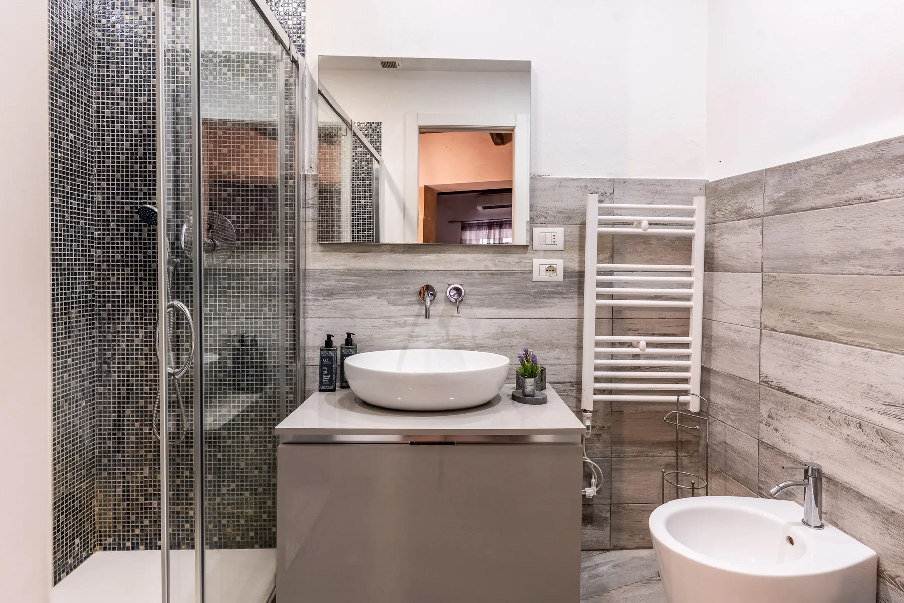 Un baño moderno con ducha de vidrio, lavabo y radiador toallero blanco.