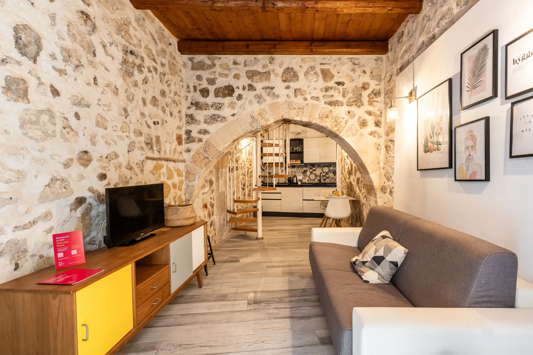 Una sala de estar con paredes de piedra, un sofá y un arco que da a la cocina.