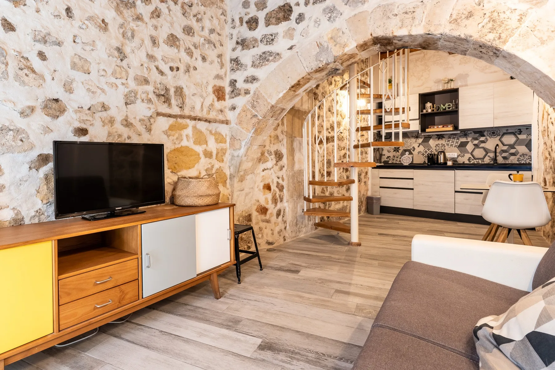 Una sala con paredes de piedra se abre a una cocina bajo un amplio arco de piedra.