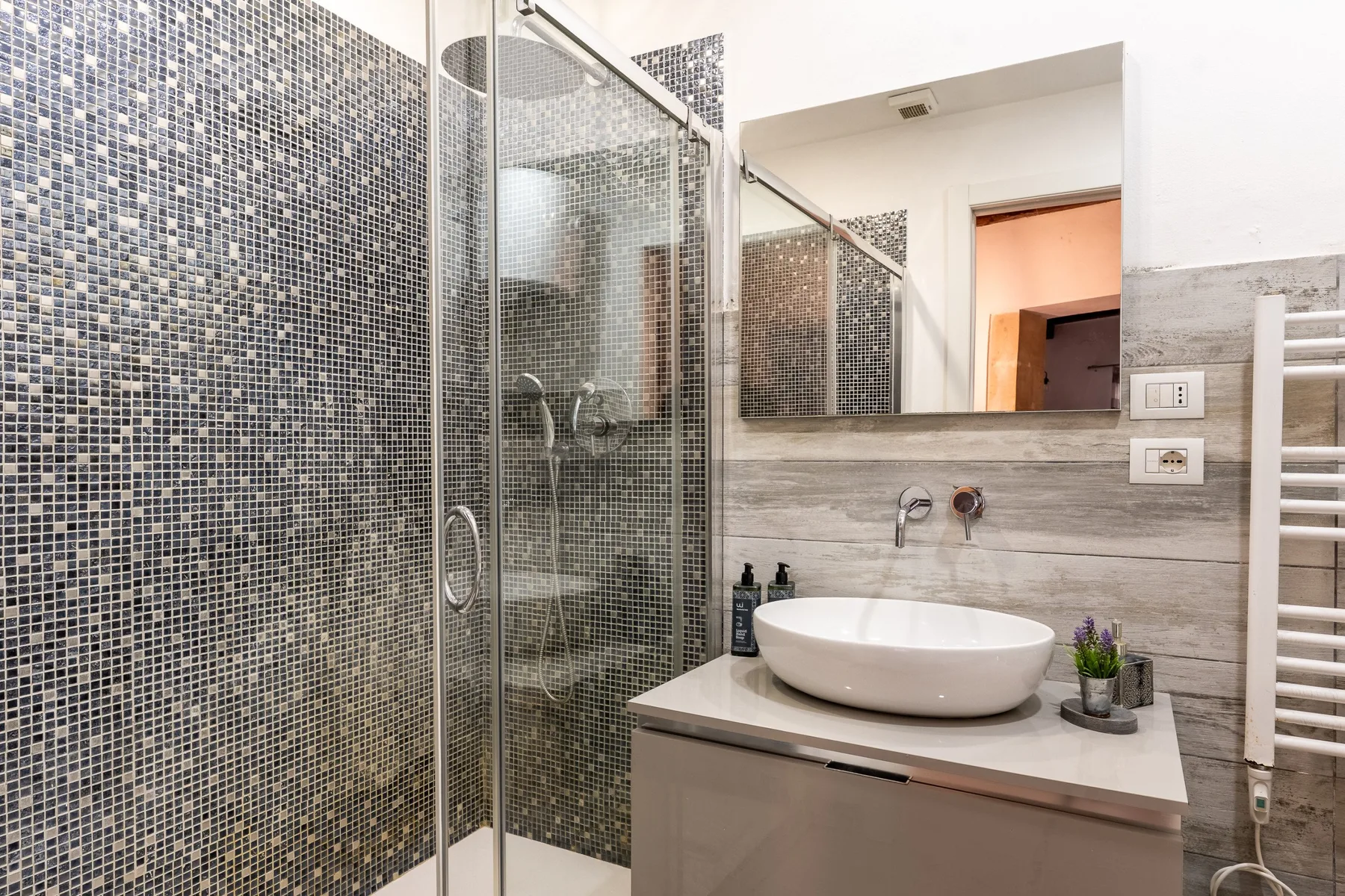 Un baño con azulejos, una ducha de vidrio y un lavabo bajo un espejo.