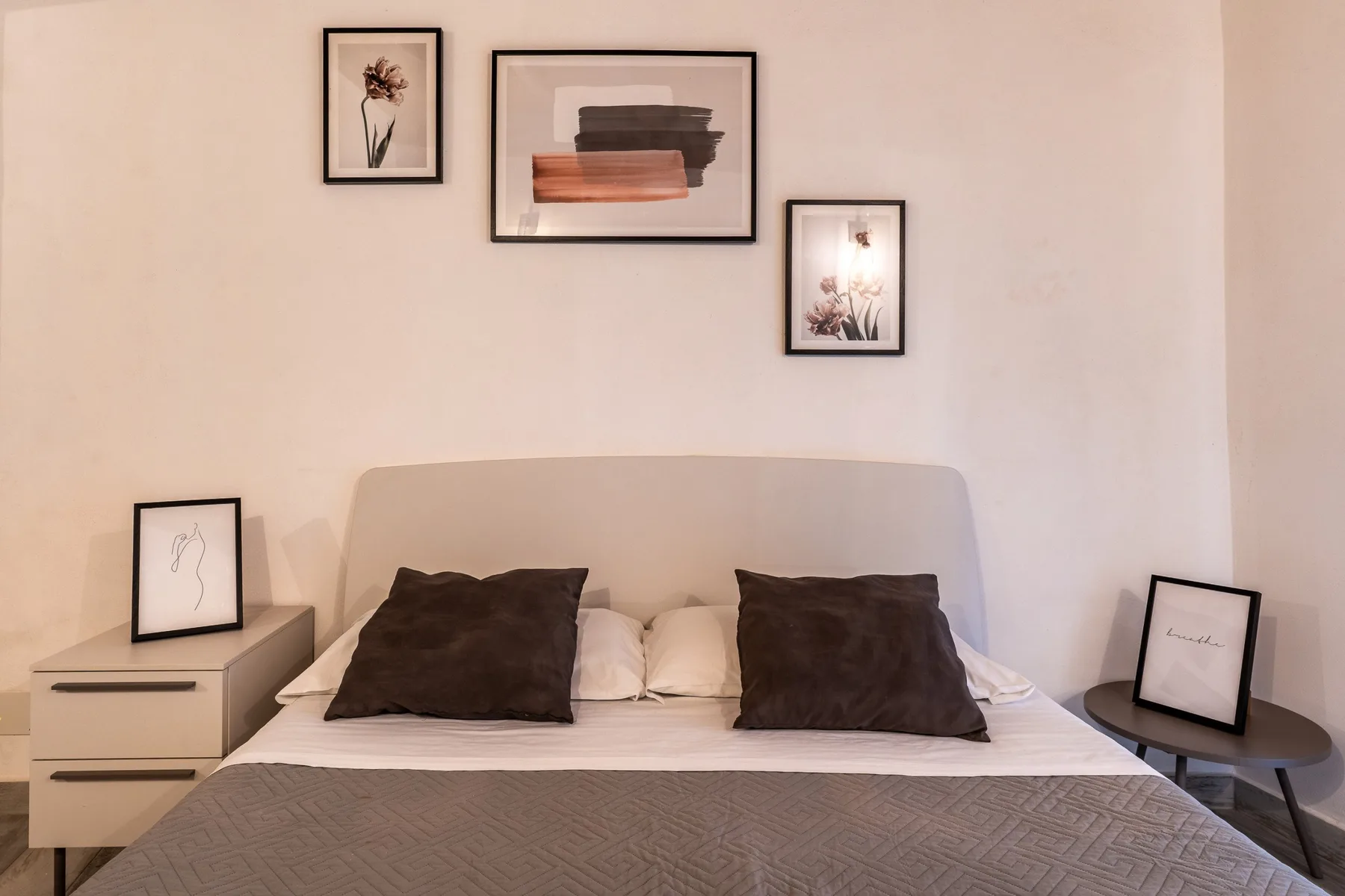 Un dormitorio con una cama tendida y cuadros enmarcados en la pared.
