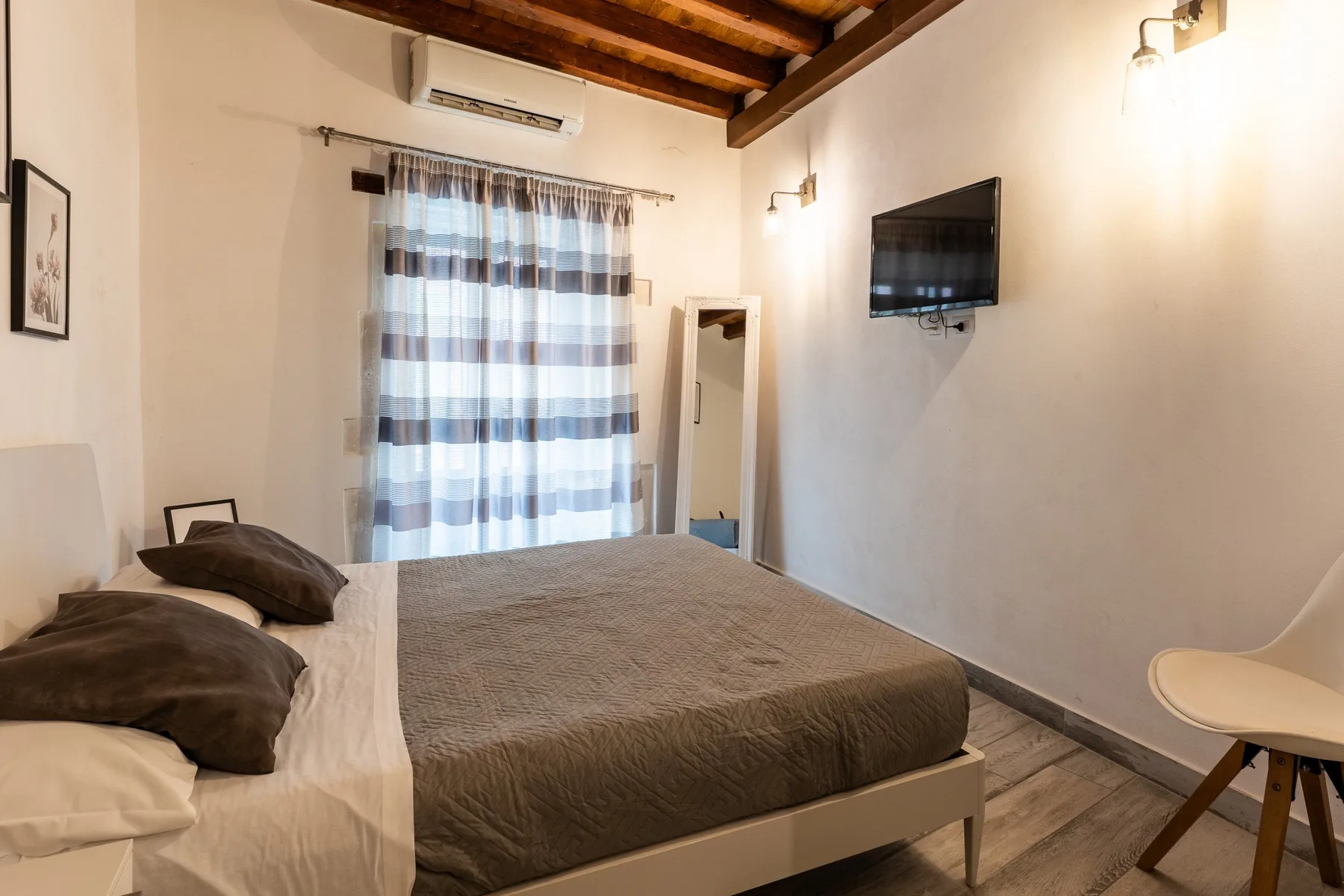 Un dormitorio con una cama, cortinas a rayas y un televisor montado en la pared.